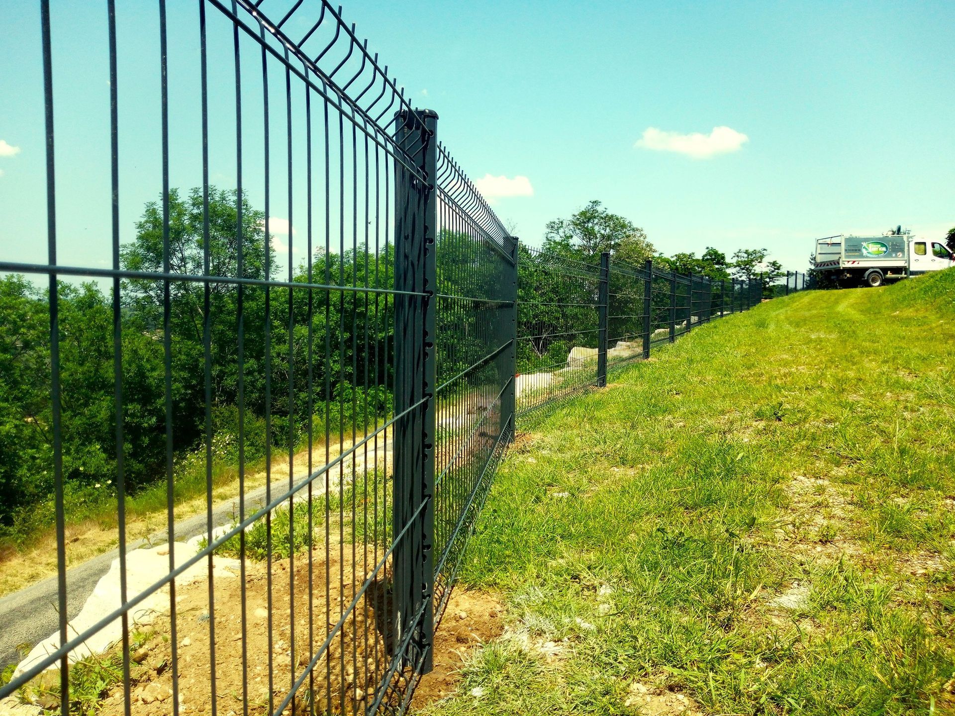 Clôture en fil de fer vert sur un fond flou d'arbres verts et de lumière du soleil.