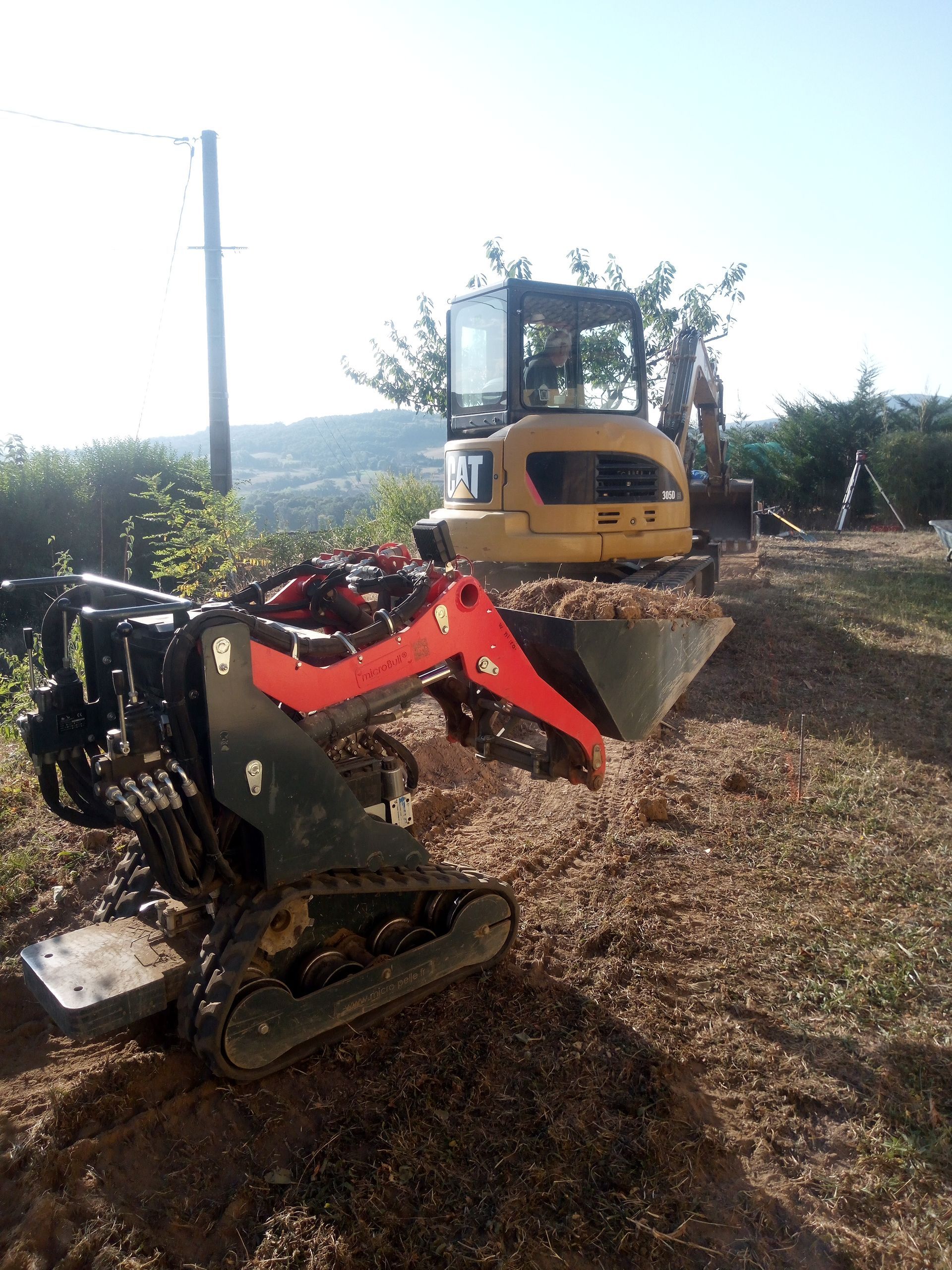 Une mini-pelle à bras rouge et une plus grande pelle jaune, sur de la terre.