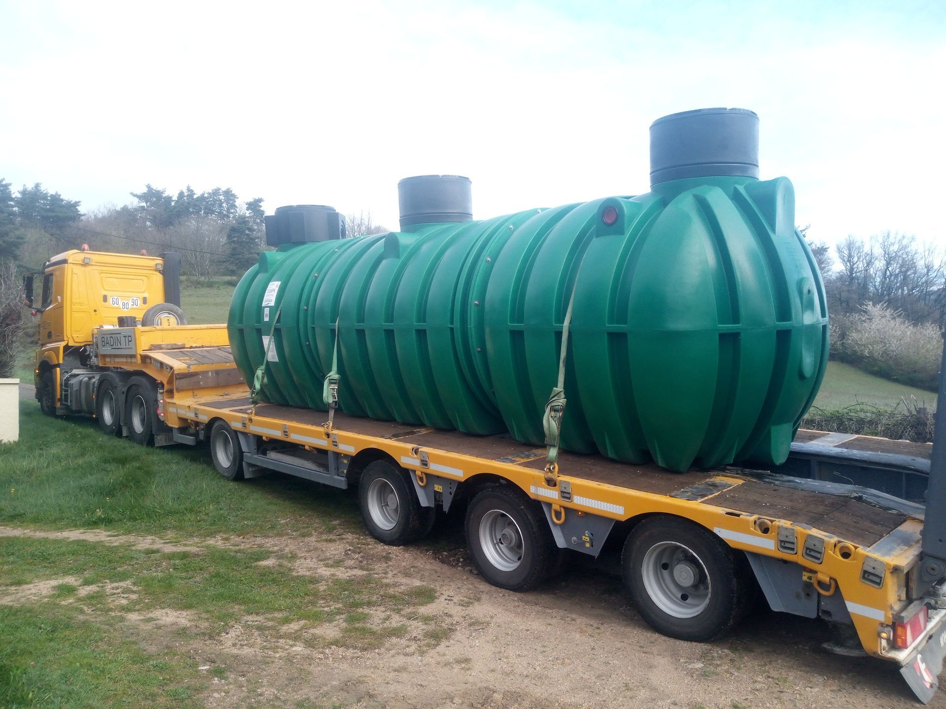 Une fosse septique verte sur un camion plateau dans un champ herbeux.