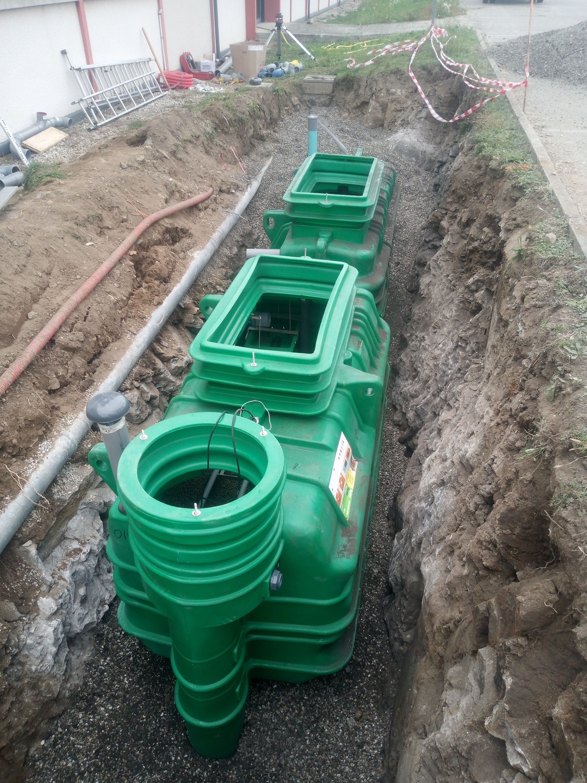 Installation d'une fosse septique verte dans une tranchée, avec couvercles d'accès ouverts.
