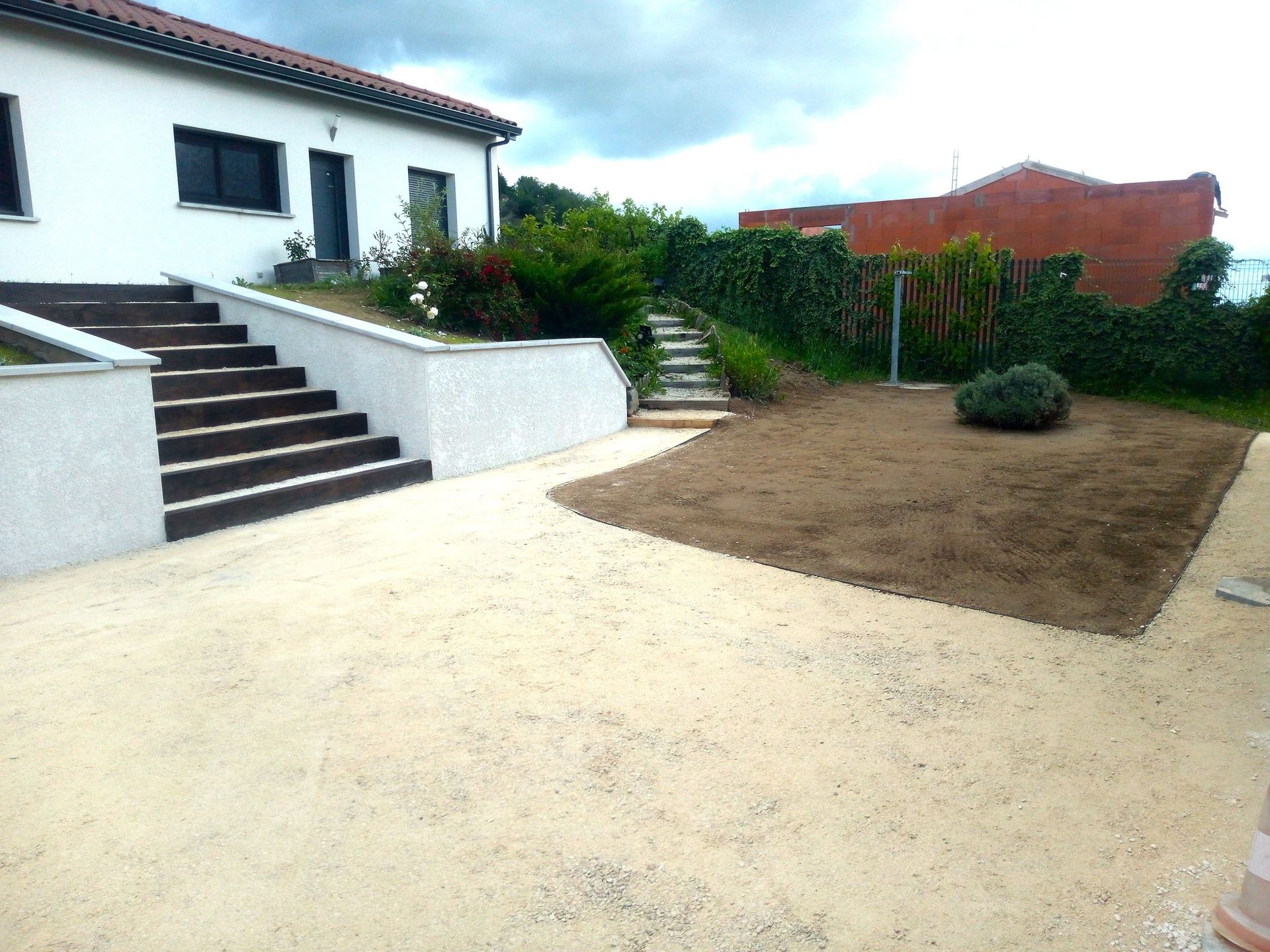 Une maison aux murs blancs, une allée de gravier, des marches et un carré d'herbe par temps nuageux.
