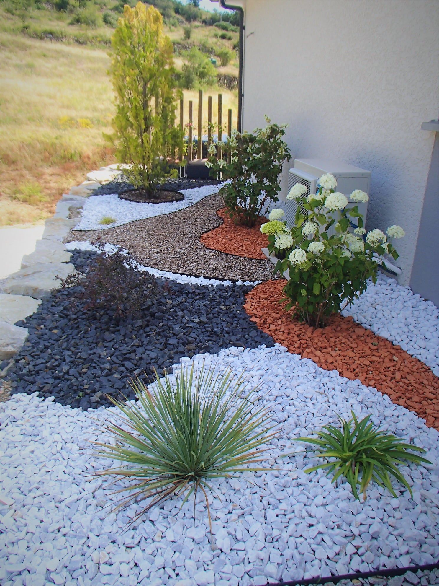 Un parterre de jardin aménagé avec des pierres et des plantes de couleurs variées devant un bâtiment blanc.