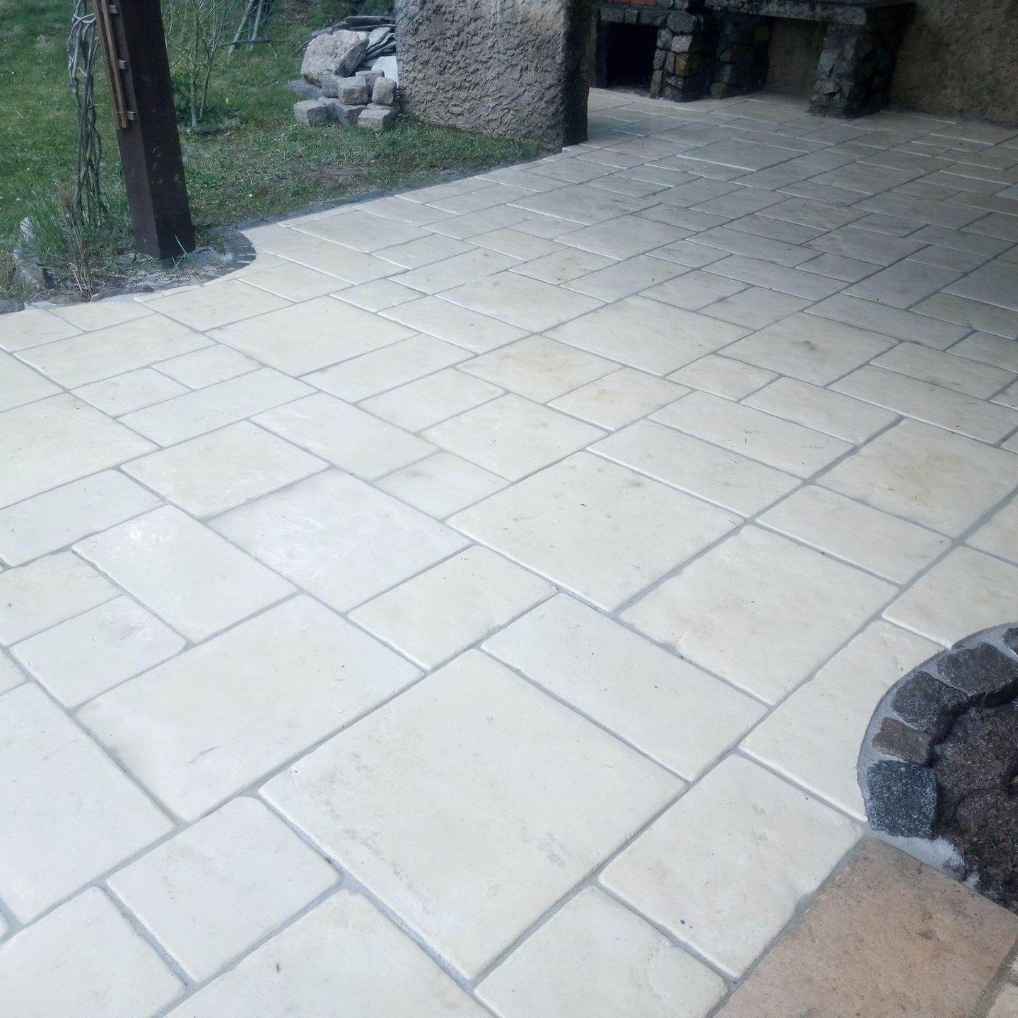 Terrasse en pierre avec des dalles rectangulaires claires et une cheminée en pierre en arrière-plan.