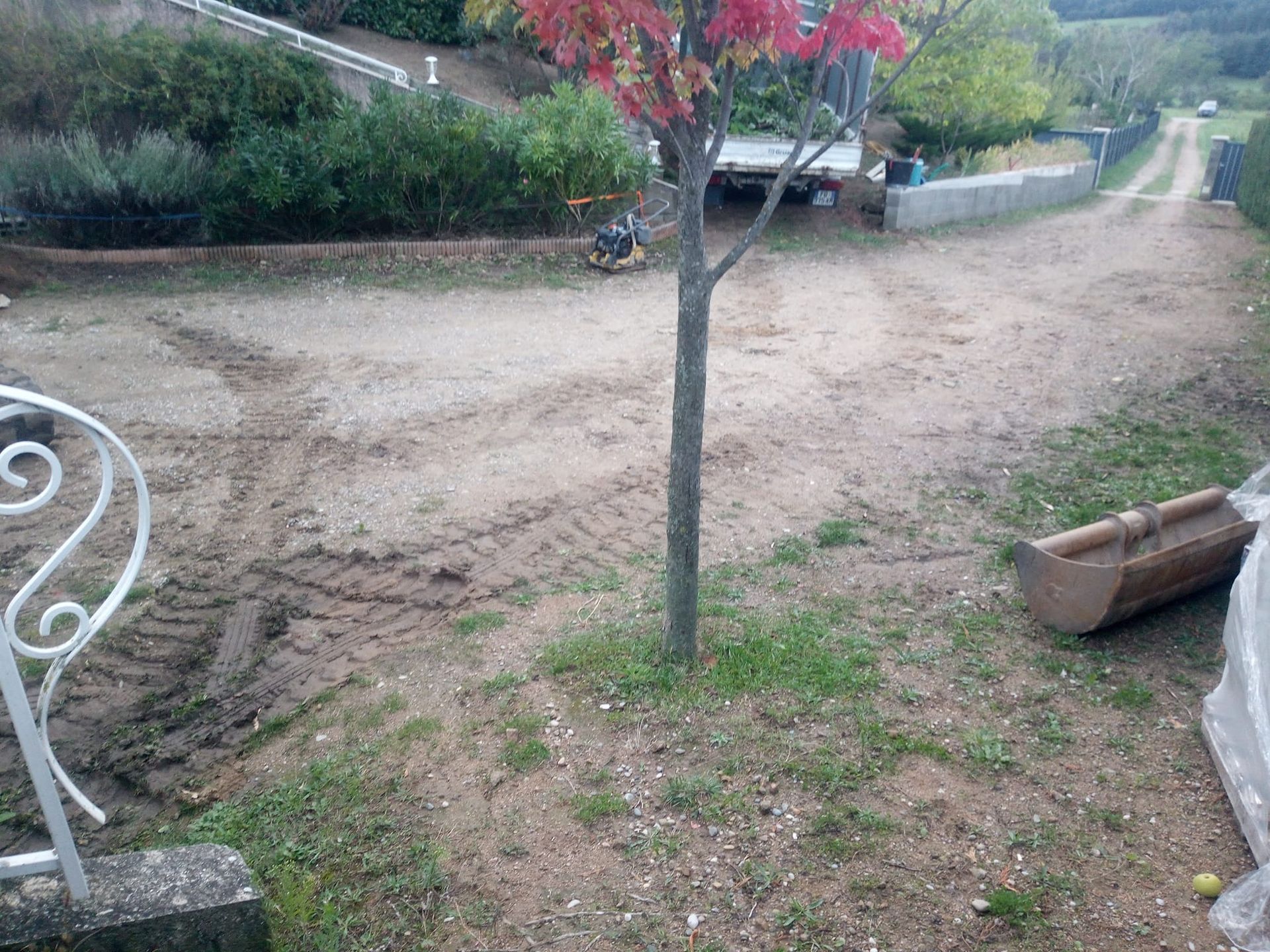 Allée en terre battue avec arbre, herbe et engins de chantier.