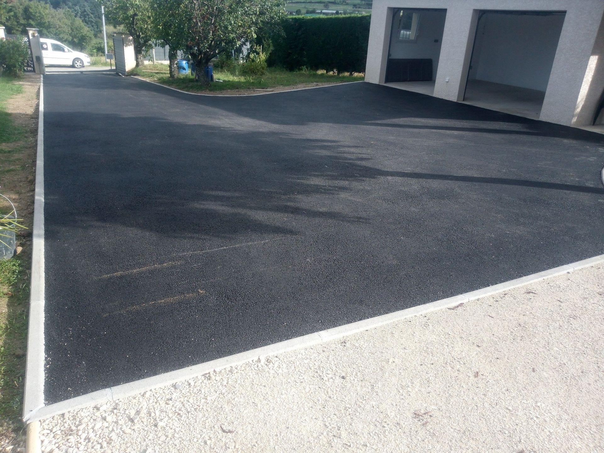 Chemin de terre avec un arbre, un véhicule et du matériel de jardinage. Feuillage rouge et vert.