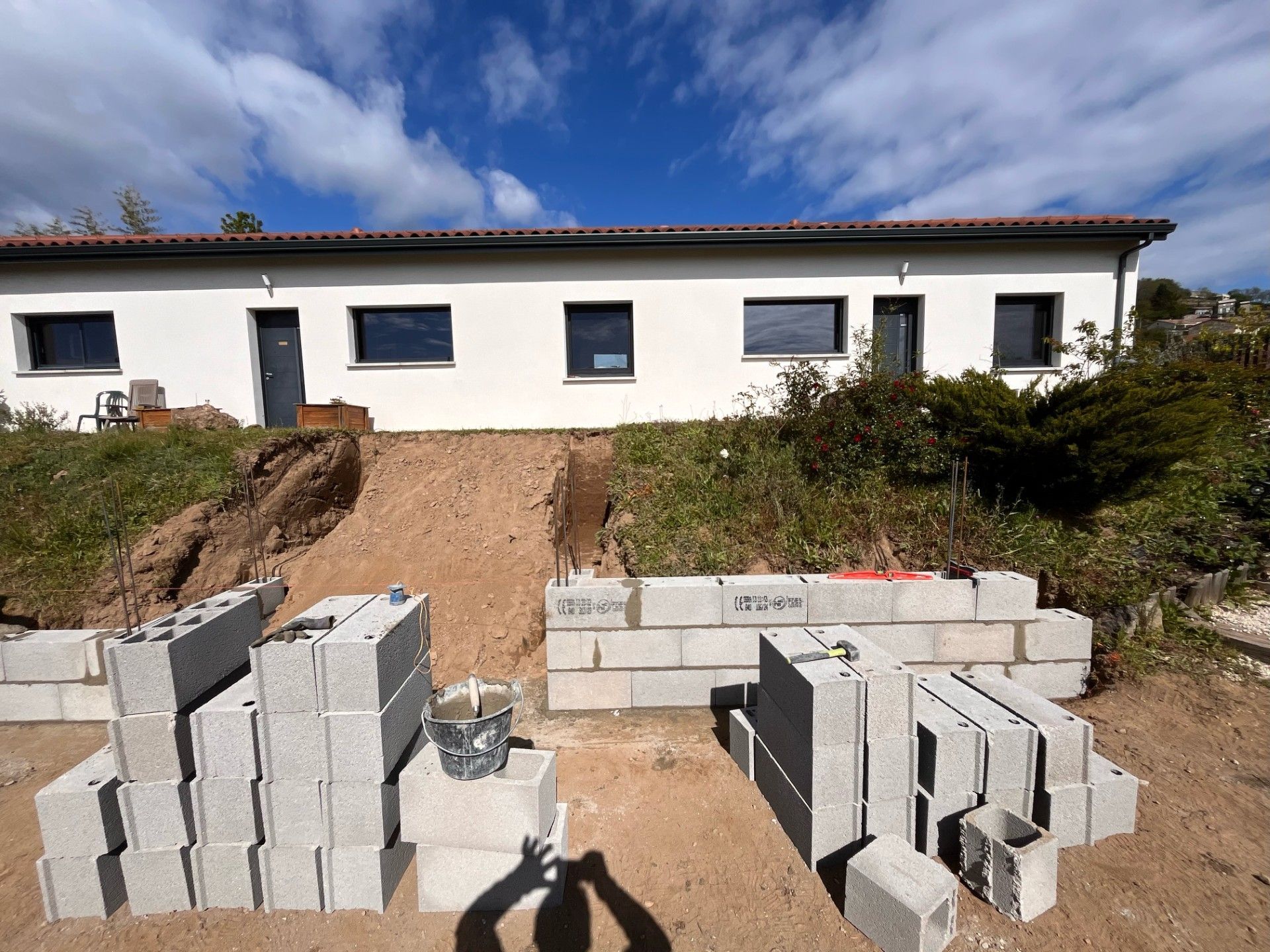 Chantier de construction avec des blocs de béton devant un bâtiment blanc, sous un ciel bleu.