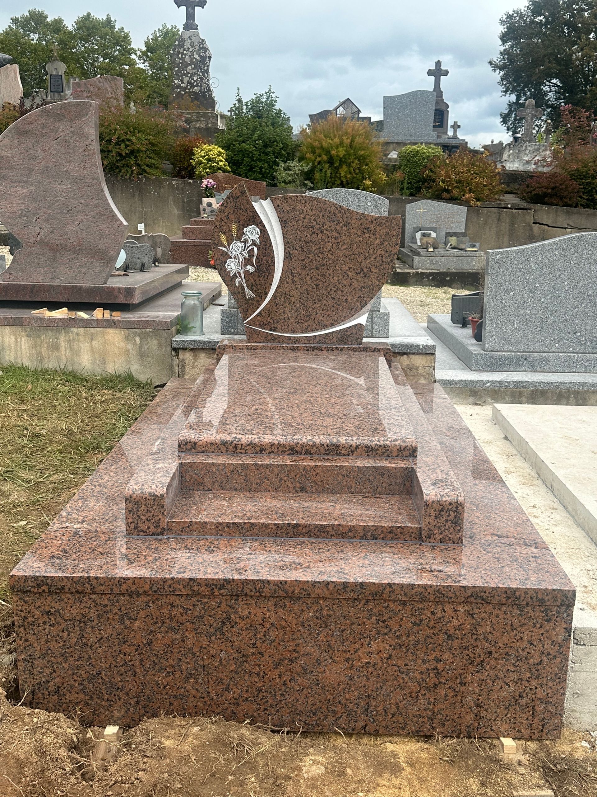 Une tombe funéraire en granit entourée d'autres monuments et d'arbres.