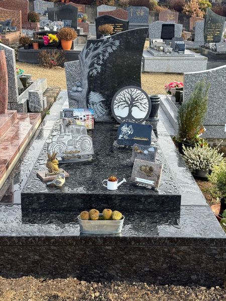 Une pierre tombale moderne en granit noir décorée de fleurs et de petits ornements, dans un cimetière.