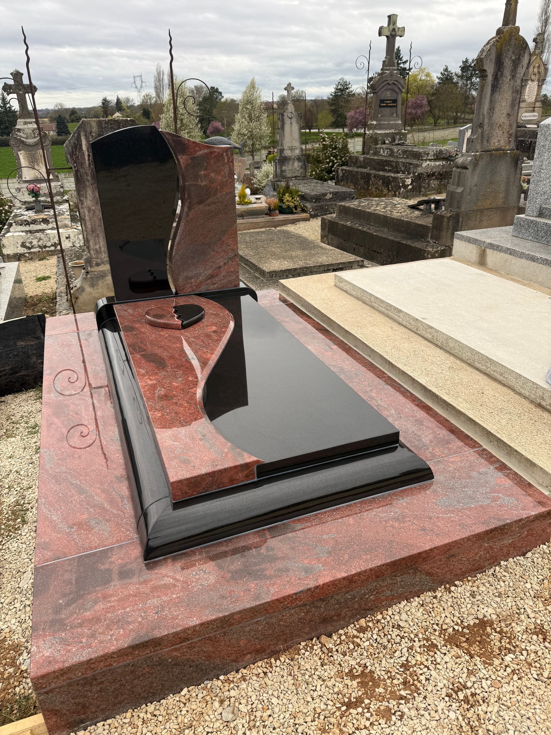 Une sépulture en granit avec un cœur sur la pierre tombale, dans un cimetière.