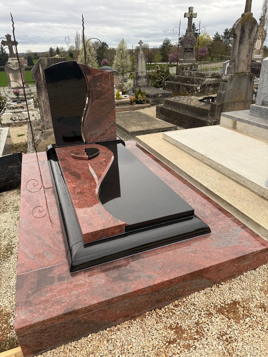 Une sépulture en granit avec un cœur sur la pierre tombale, dans un cimetière.