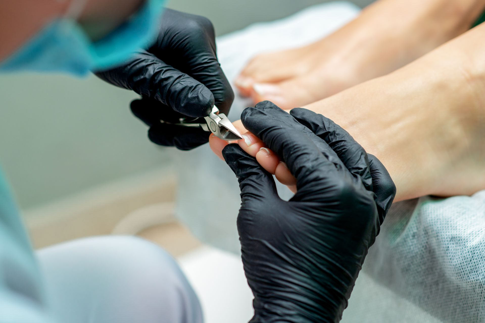 Une personne portant des gants noirs se coupe les ongles des orteils.