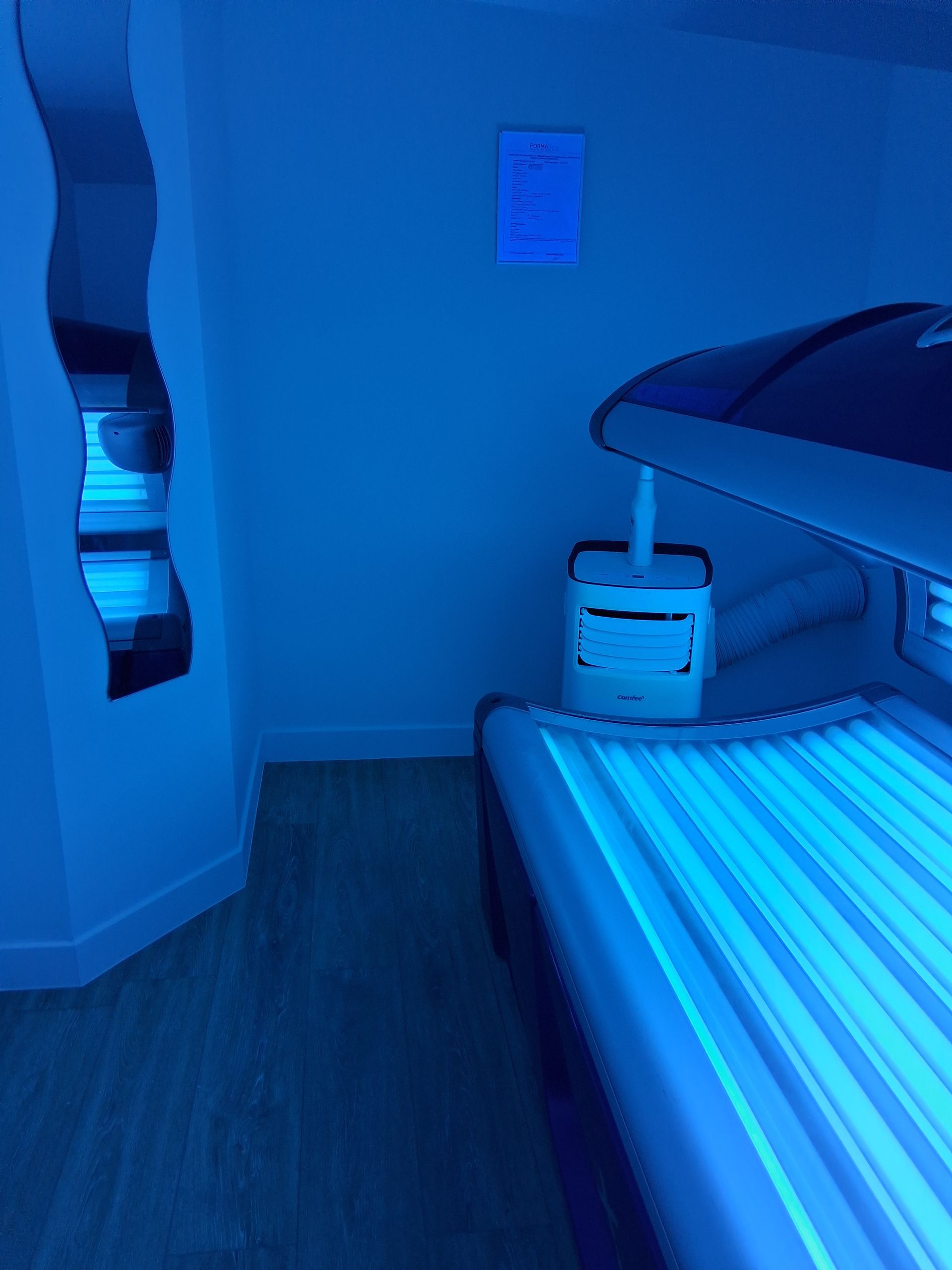 Lit de bronzage dans une pièce lumineuse éclairée en bleu, avec un miroir ondulé sur le mur et un panneau.