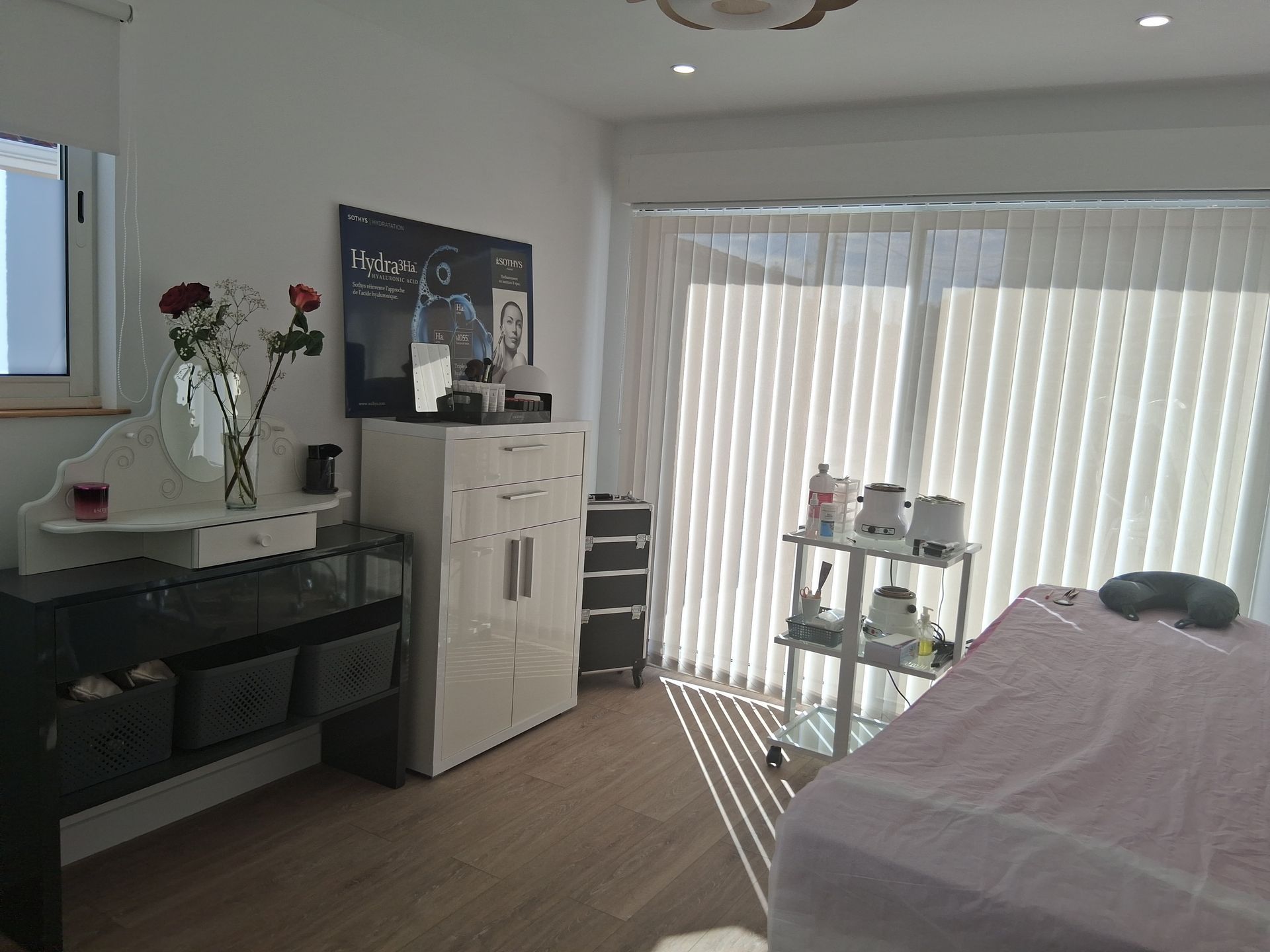 Espace spa avec table de massage, coiffeuse et meuble de rangement. Pièce lumineuse aux murs blancs.