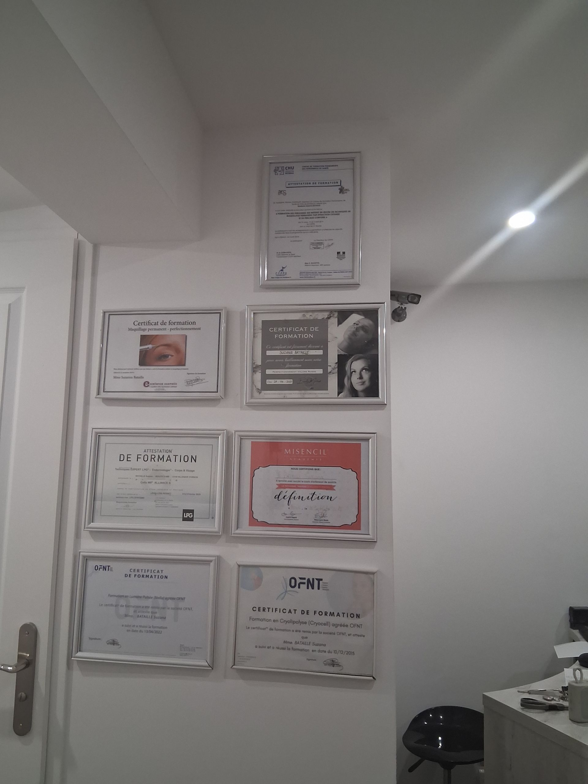 Certificats dans des cadres argentés sur un mur blanc ; une porte est visible sur la gauche.