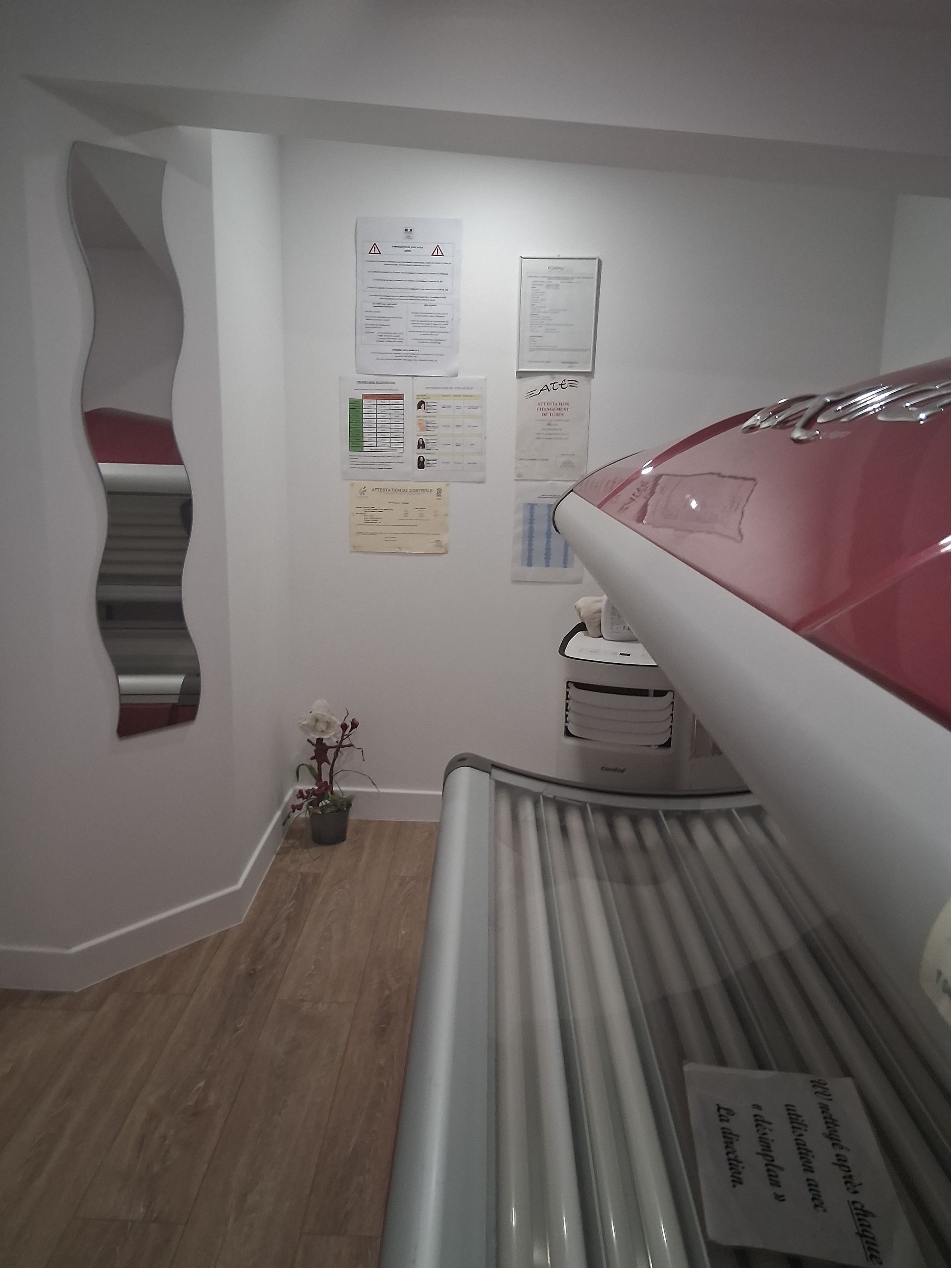 Lit de bronzage dans une pièce blanche, avec des documents au mur et un miroir ondulé.