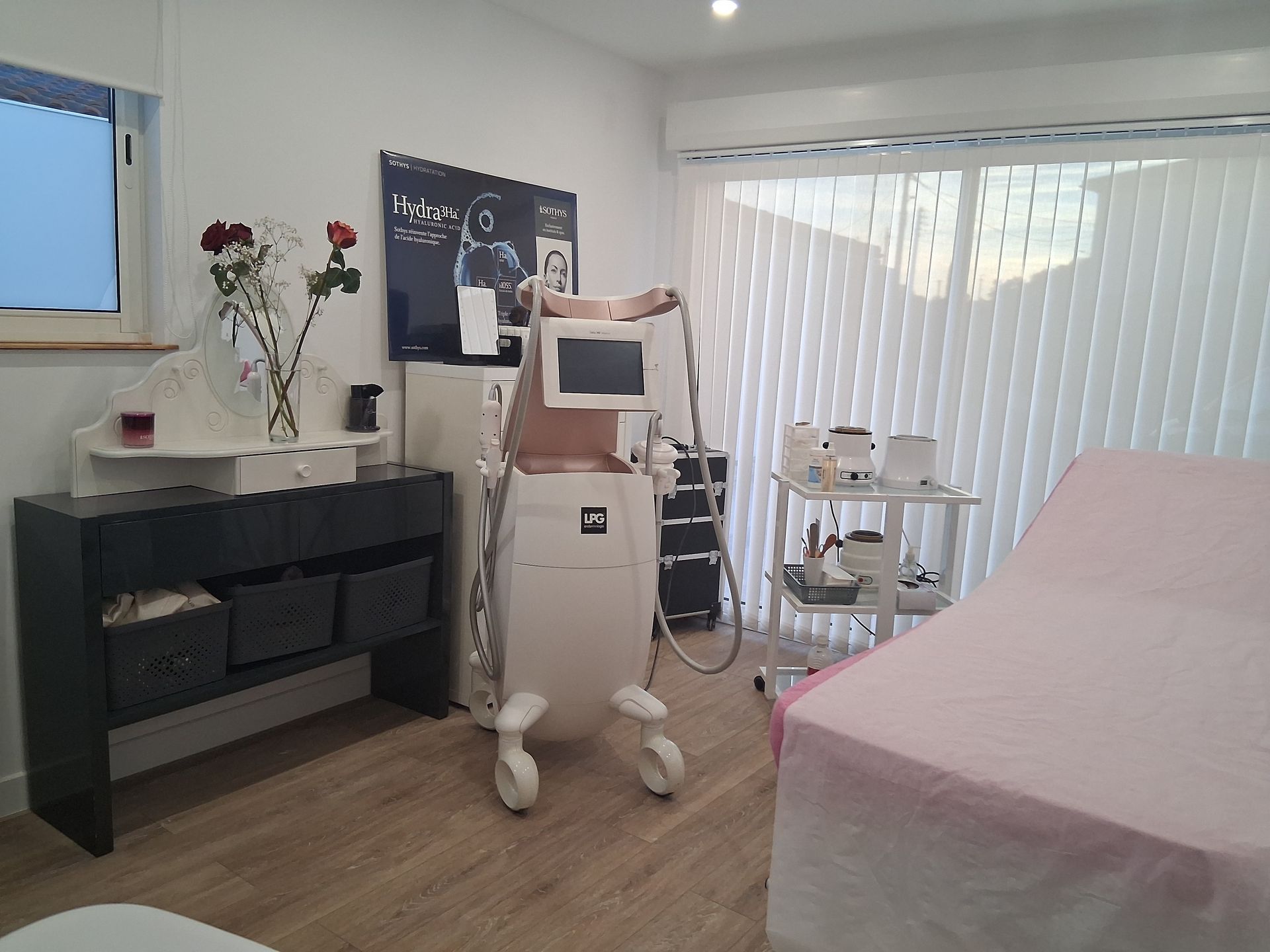 Une salle médicale avec une machine laser, un lit de traitement et une coiffeuse avec des fleurs.