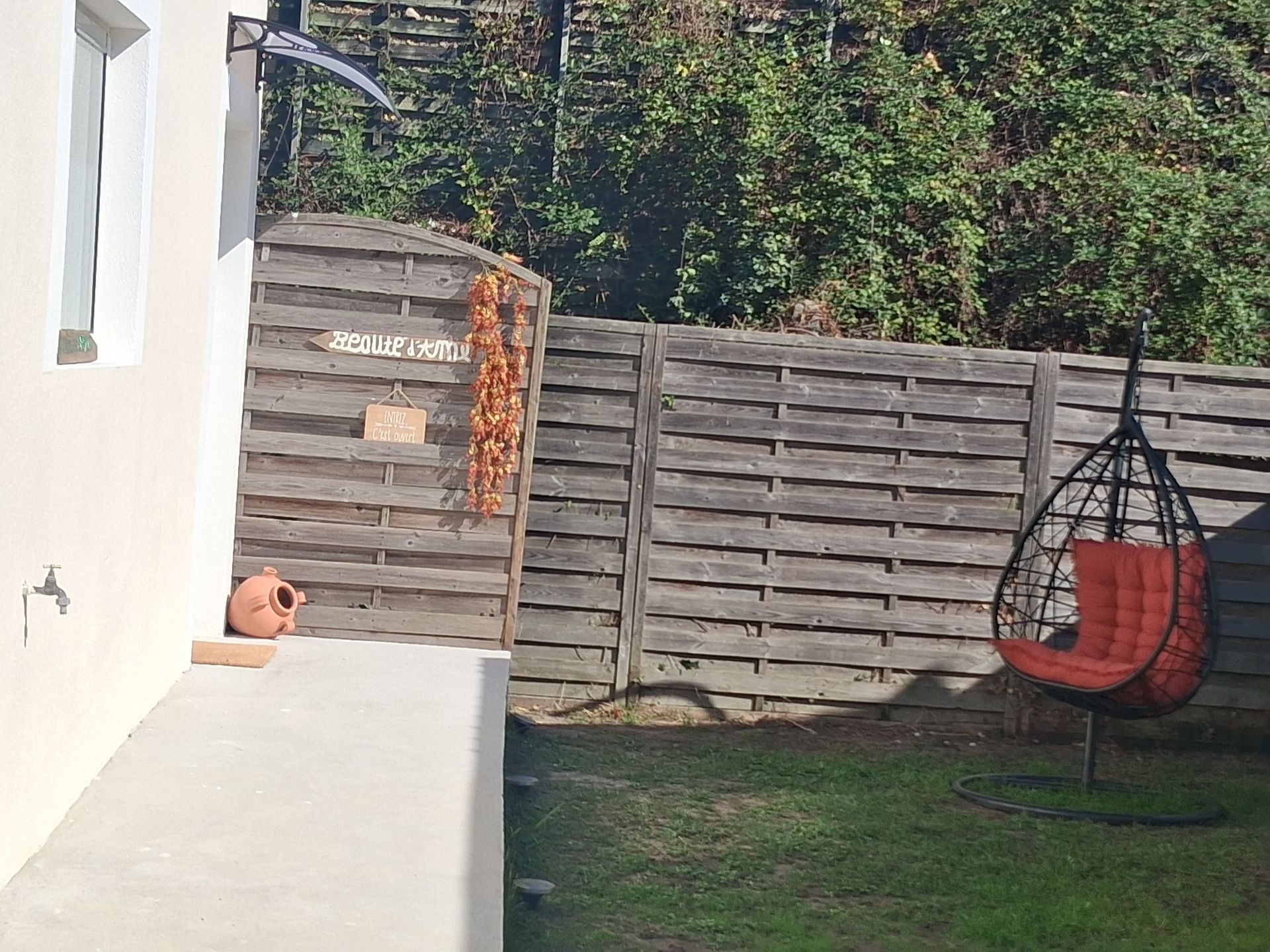 Un jardin avec une clôture, une chaise suspendue et un bâtiment. La chaise est rouge.