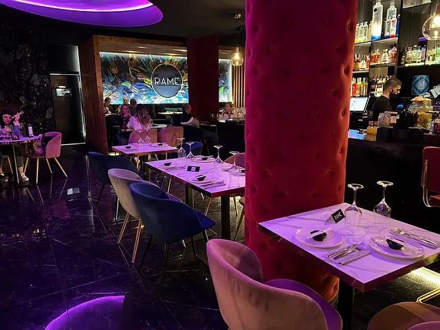 Un restaurante con mesas y sillas y luces violetas.