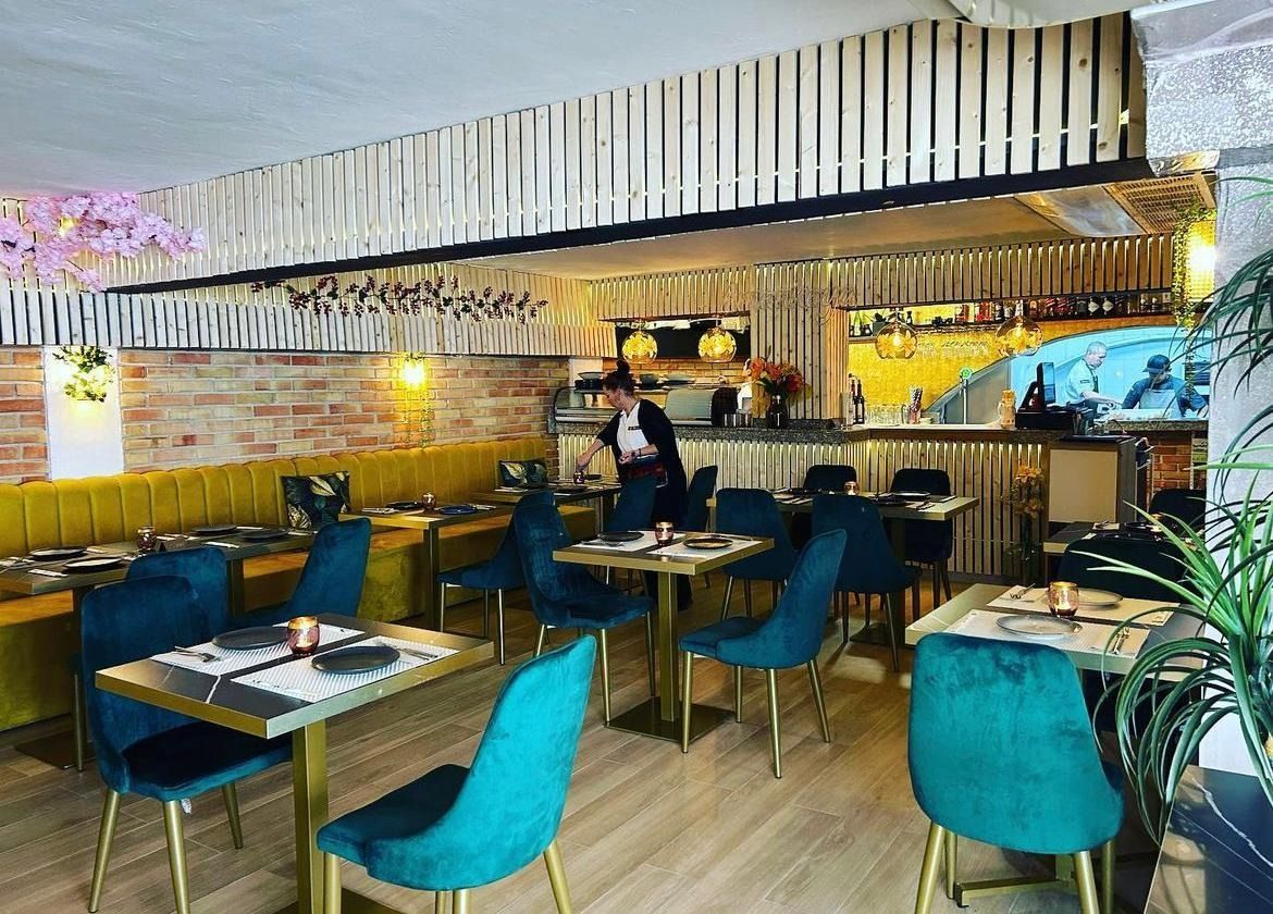 Un restaurante con mesas y sillas y un hombre de pie en la cocina.