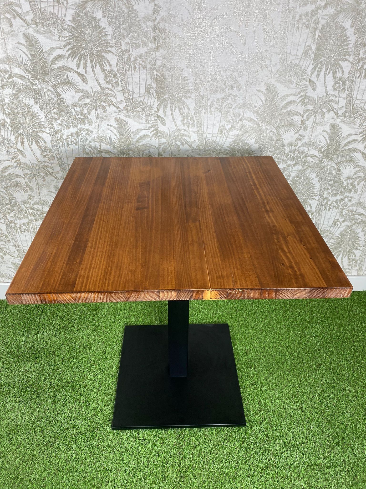 Una mesa de madera con una base negra está colocada encima de una alfombra verde.