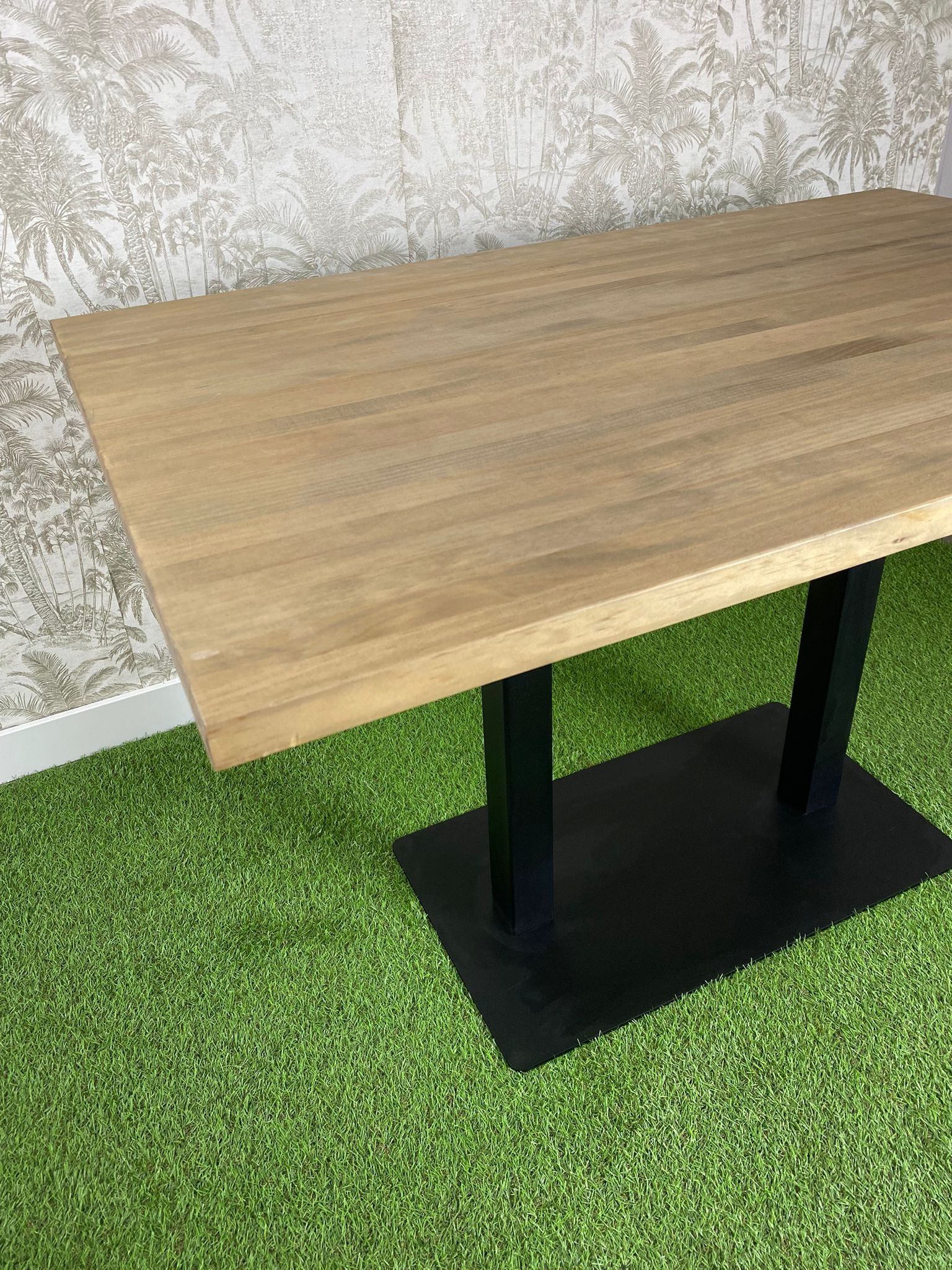Una mesa de madera con una base negra está colocada encima de una alfombra verde.