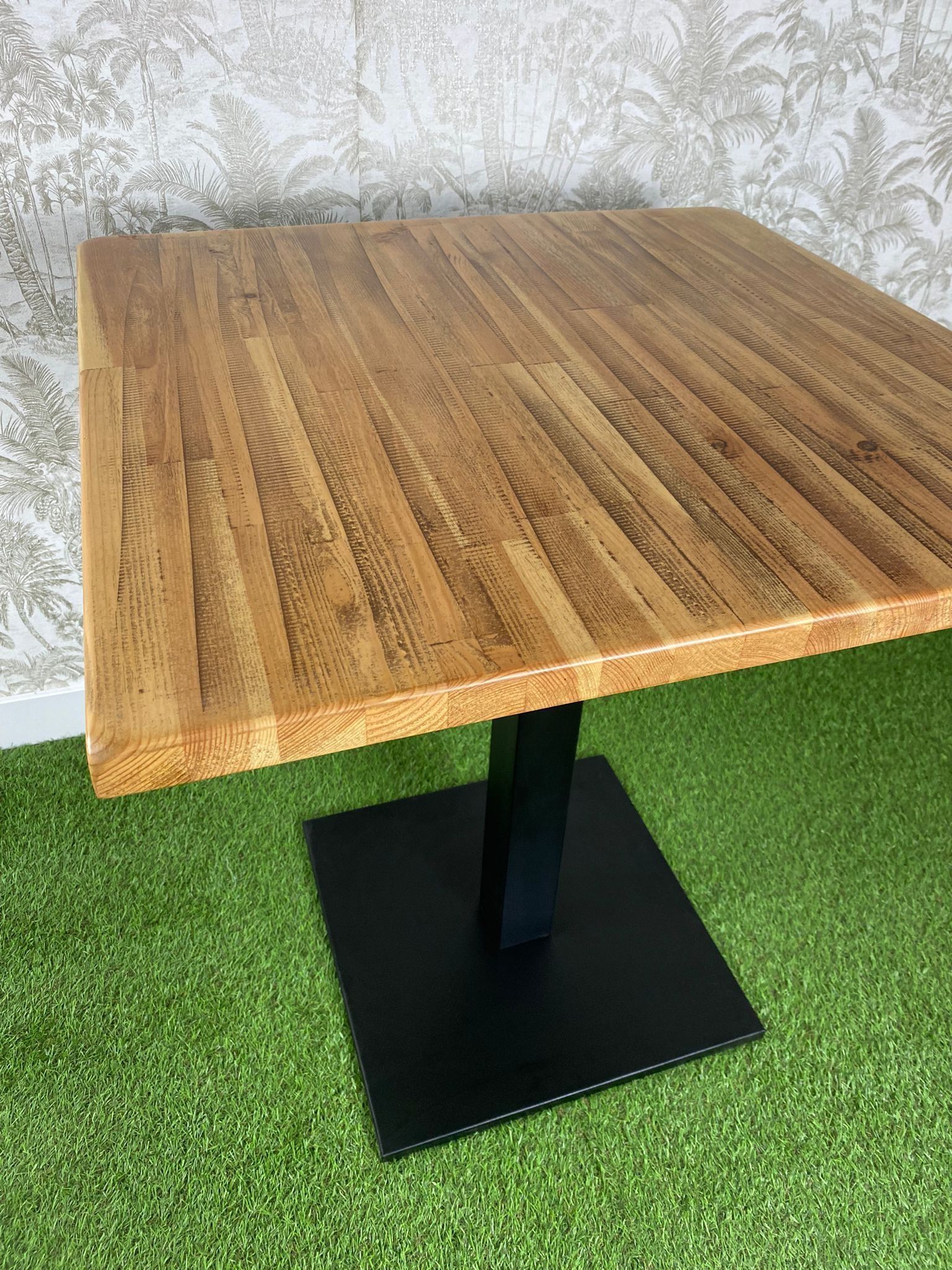 Una mesa de madera con una base negra está colocada encima de una alfombra verde.