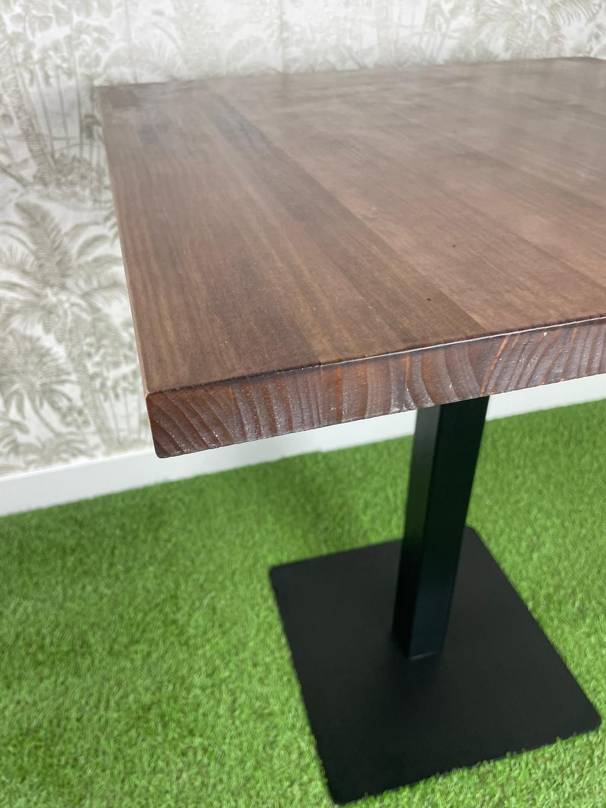 Una mesa de madera con una base negra está colocada encima de una alfombra verde.