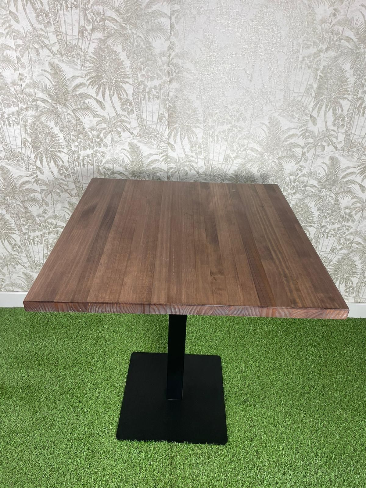 Una mesa de madera con una base negra está colocada encima de una alfombra verde.
