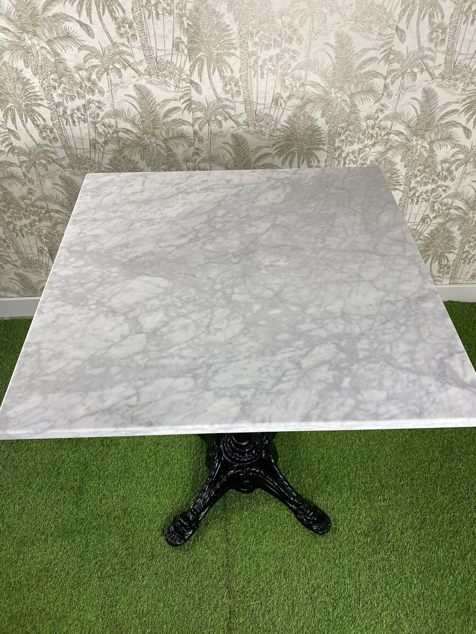 Una mesa de mármol blanco con una base negra reposa sobre una alfombra verde.