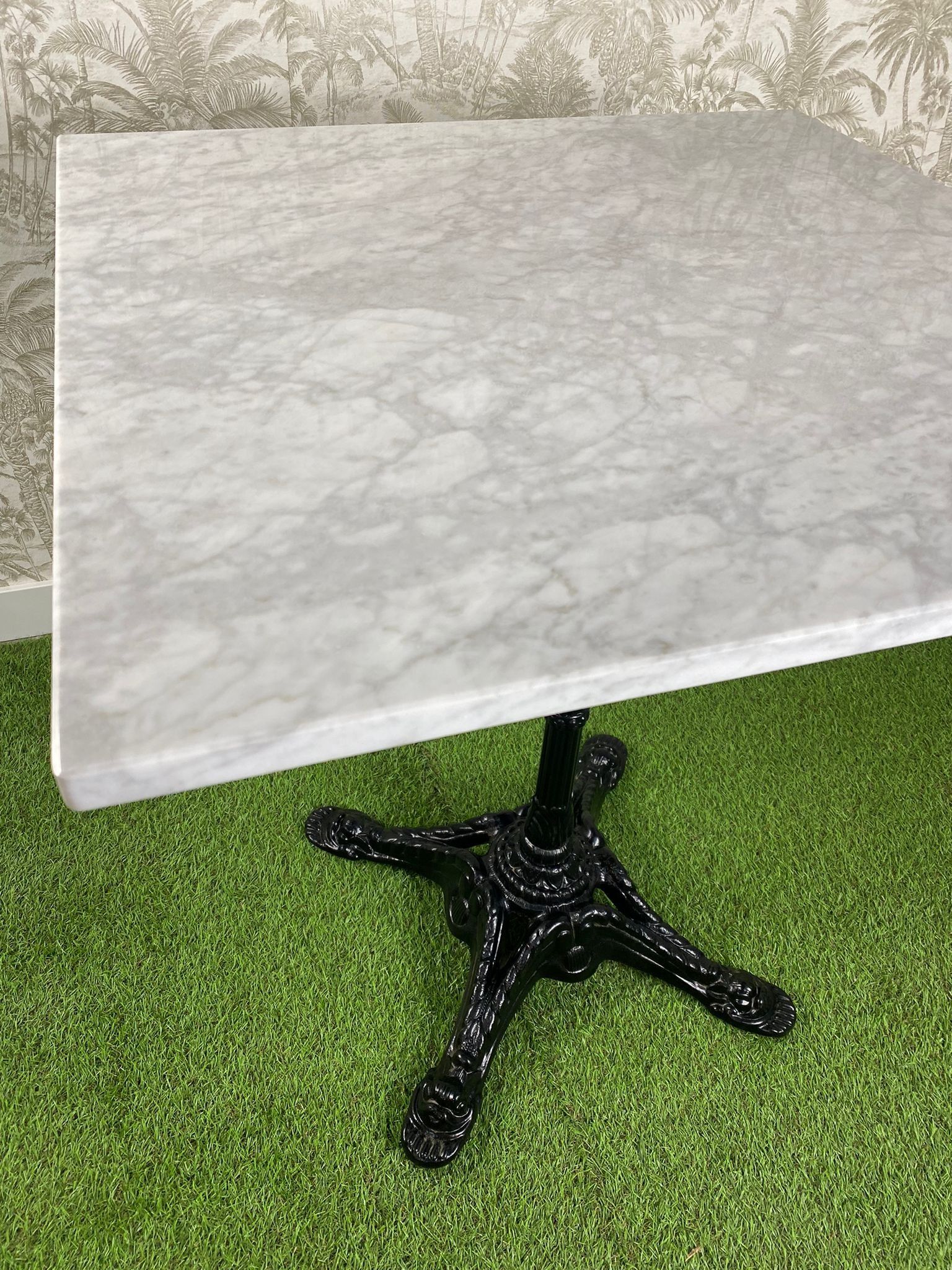 Una mesa de mármol blanco con una base negra reposa sobre una alfombra verde.