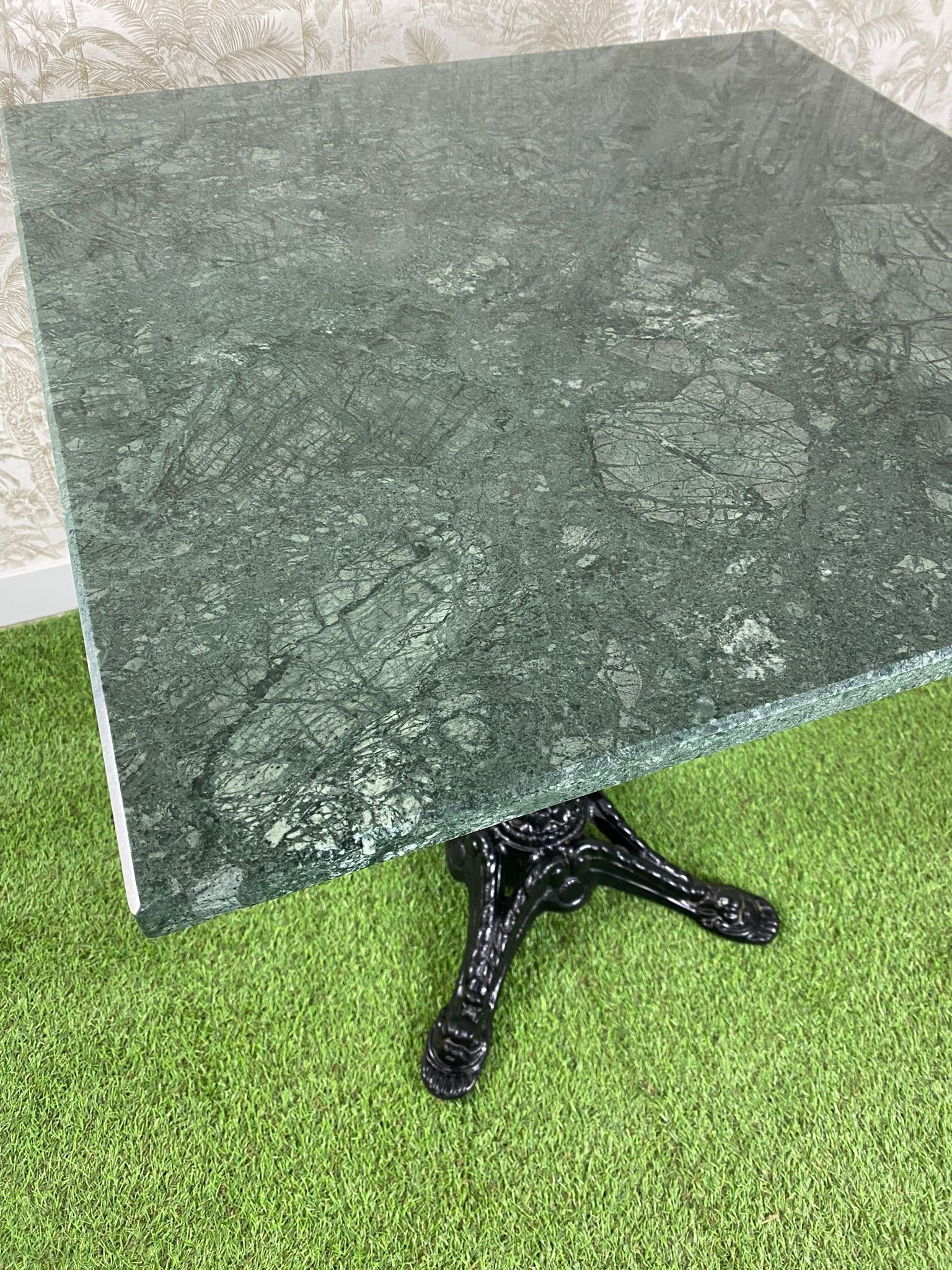 Una mesa de mármol verde con una base negra está colocada encima de una alfombra verde.