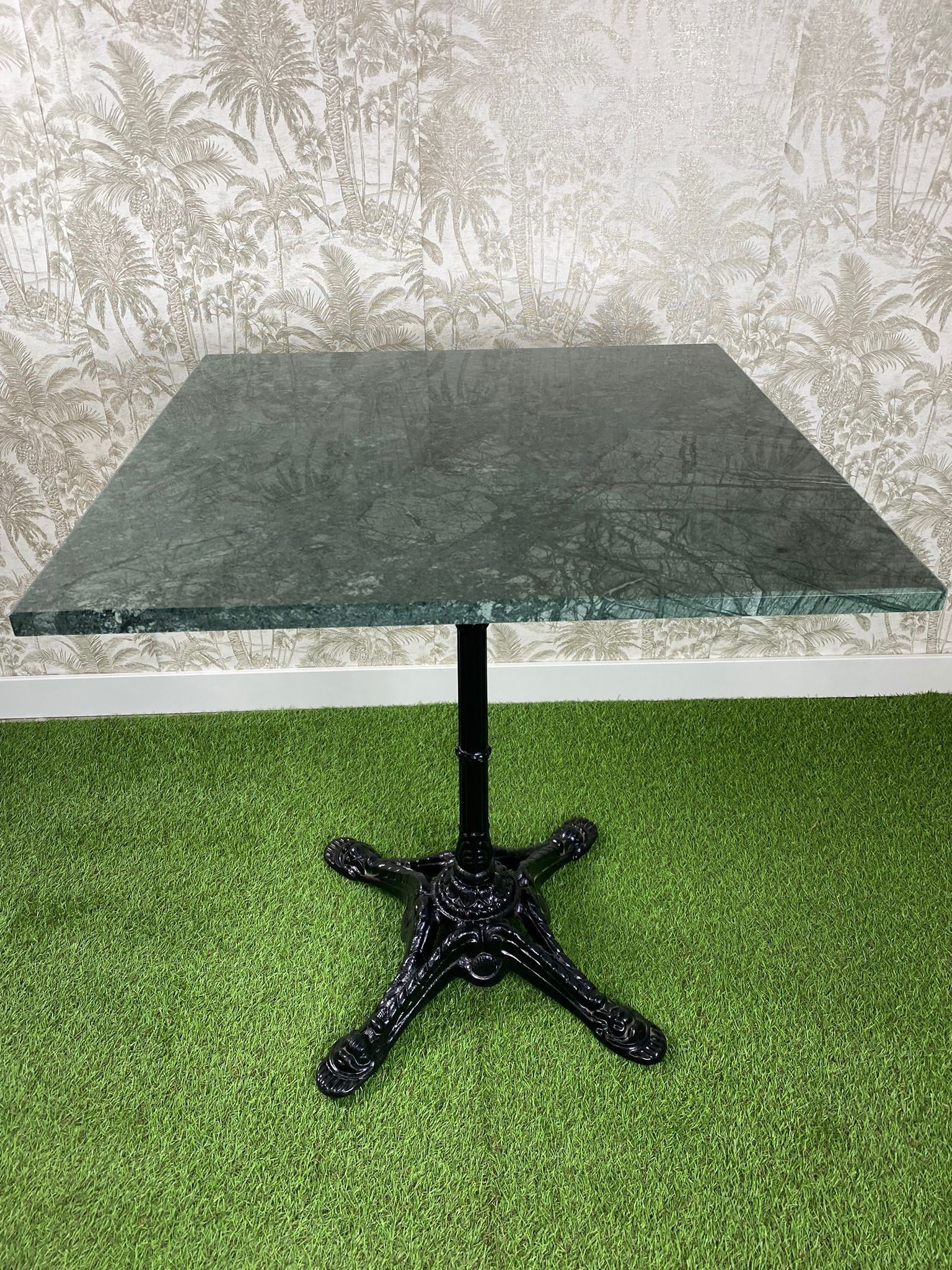 Una mesa de mármol verde con una base negra está colocada encima de una alfombra verde.