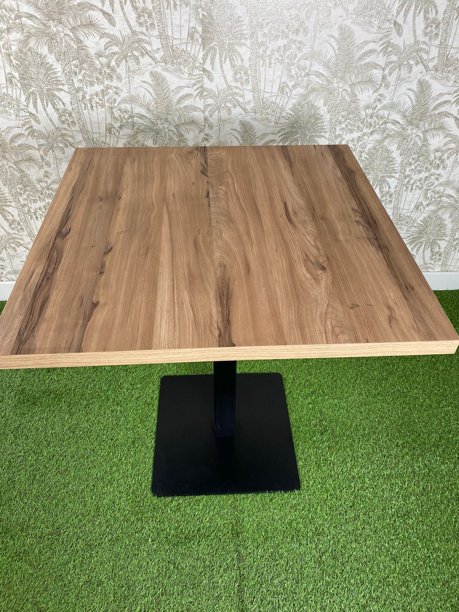 Una mesa de madera con una base negra está colocada encima de una alfombra verde.