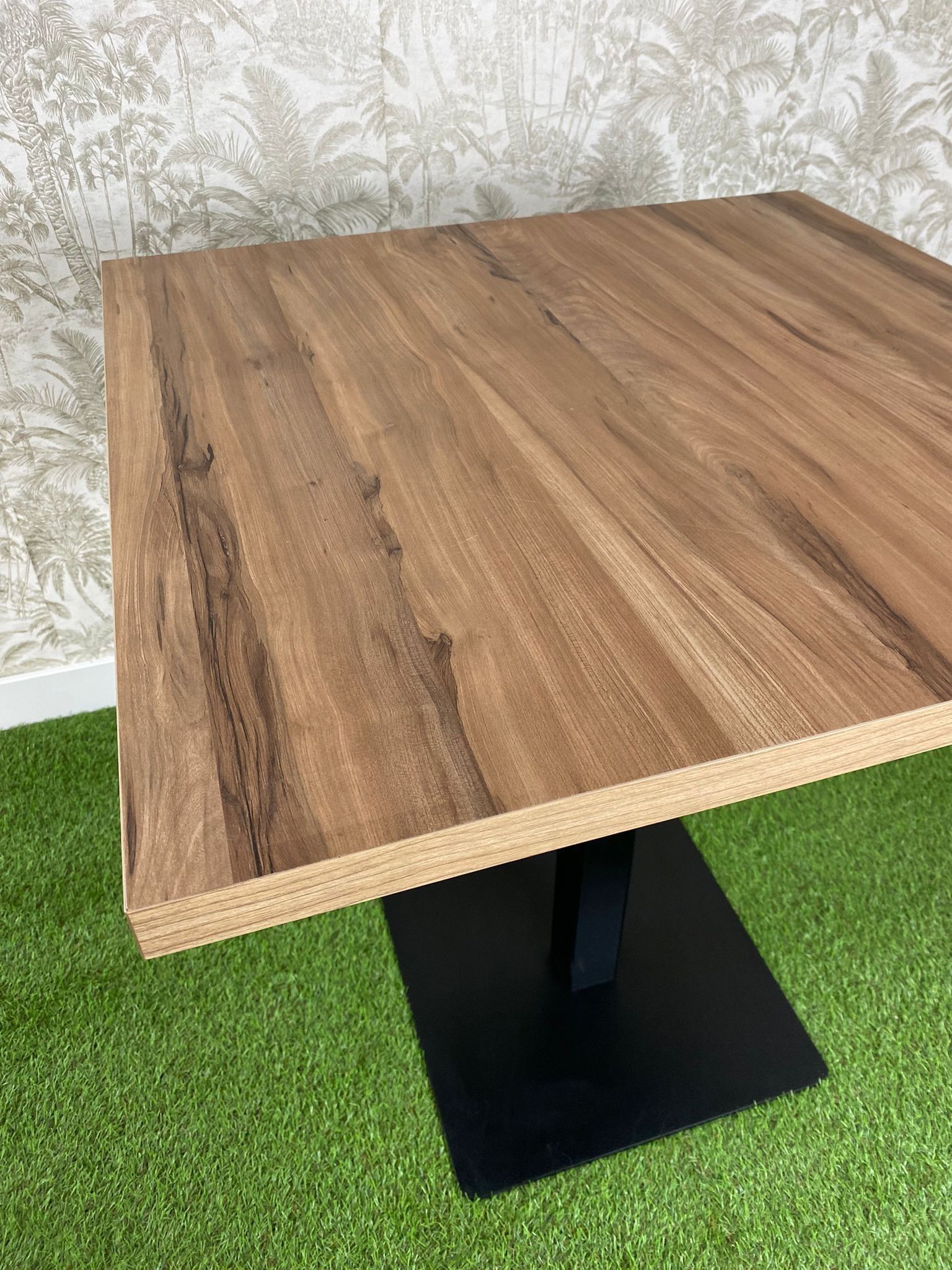 Una mesa de madera con una base negra está colocada encima de una alfombra verde.