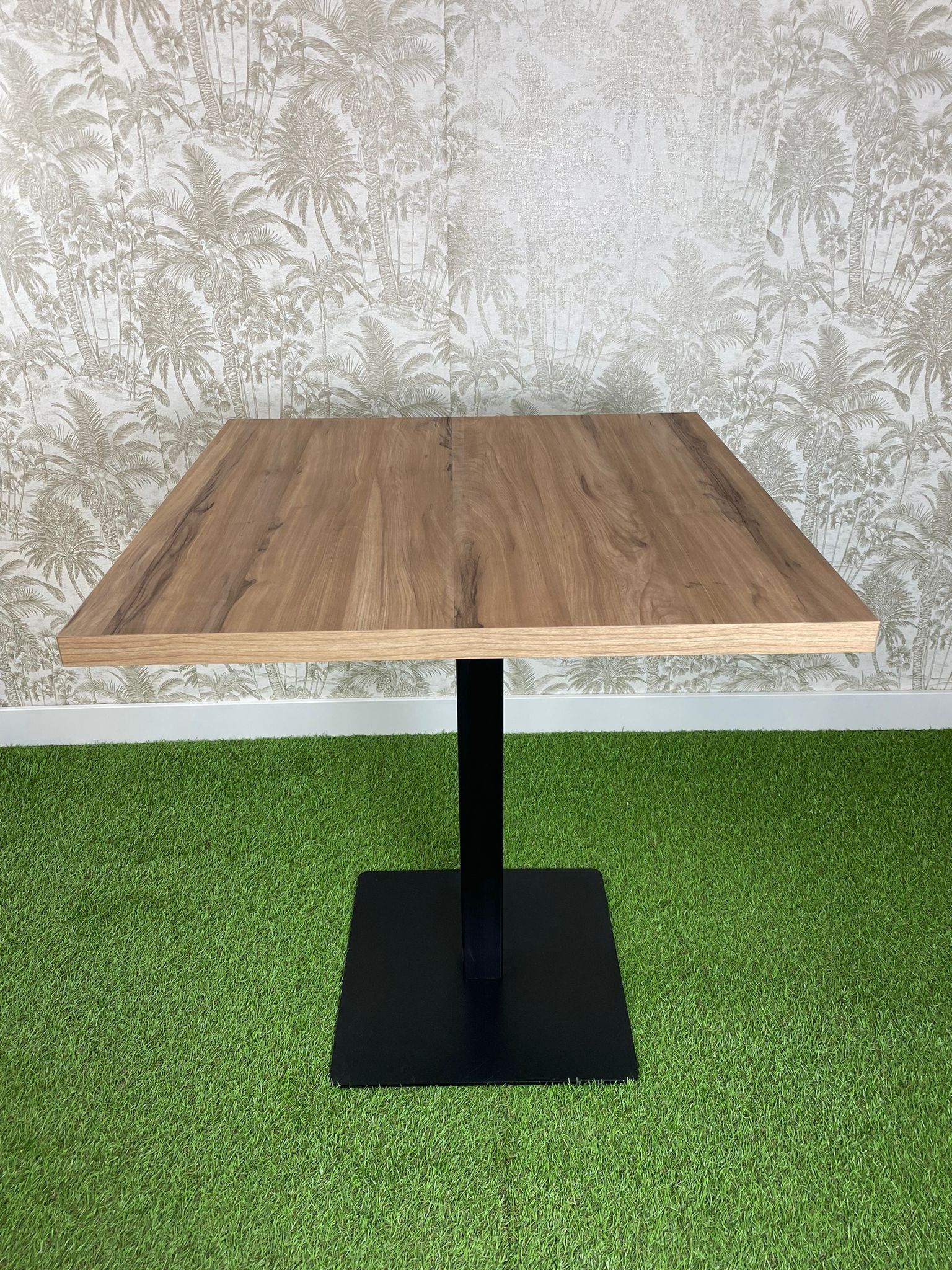 Una mesa de madera con una base negra está colocada encima de una alfombra verde.