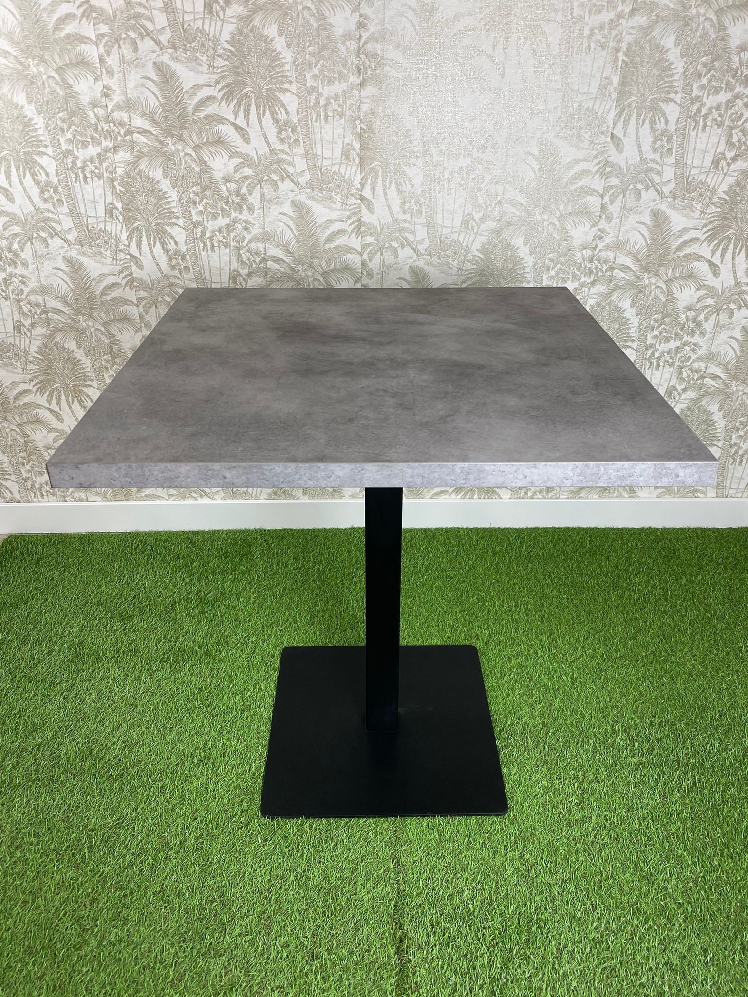 Una mesa cuadrada con una base negra se encuentra sobre un exuberante campo verde.