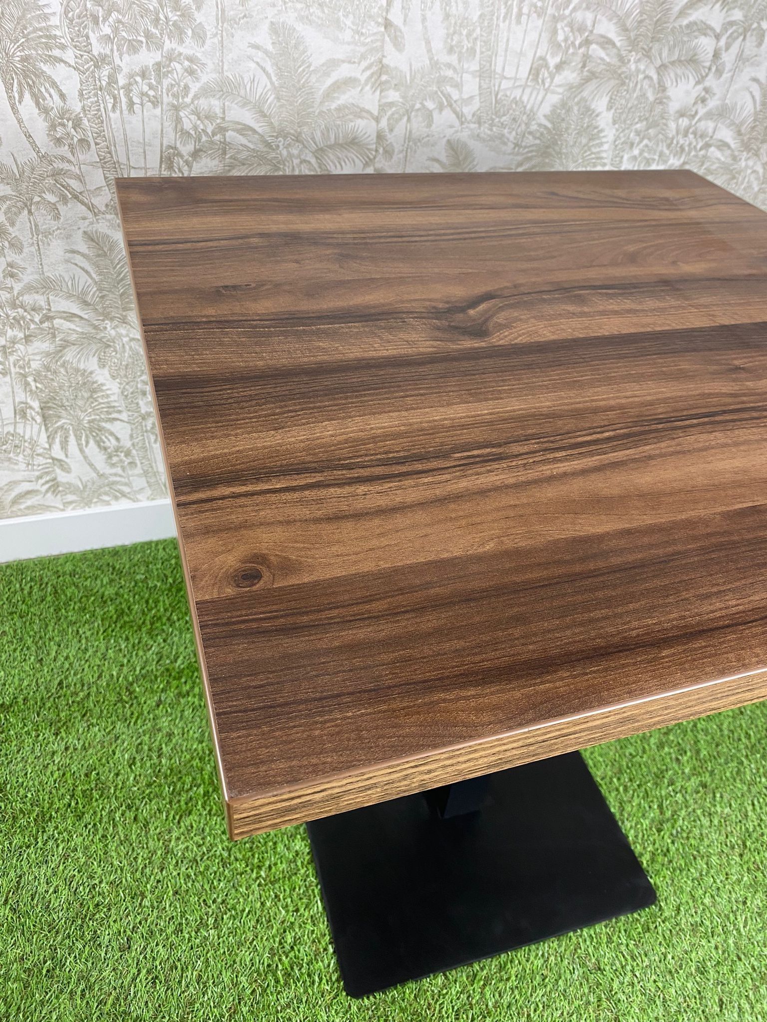 Una mesa de madera con una base negra está colocada encima de una alfombra verde.