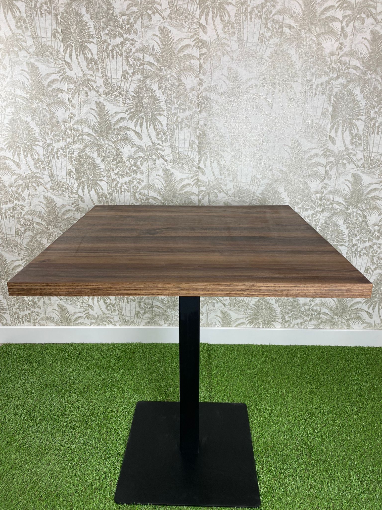 Una mesa de madera con una base negra está colocada encima de una alfombra verde.