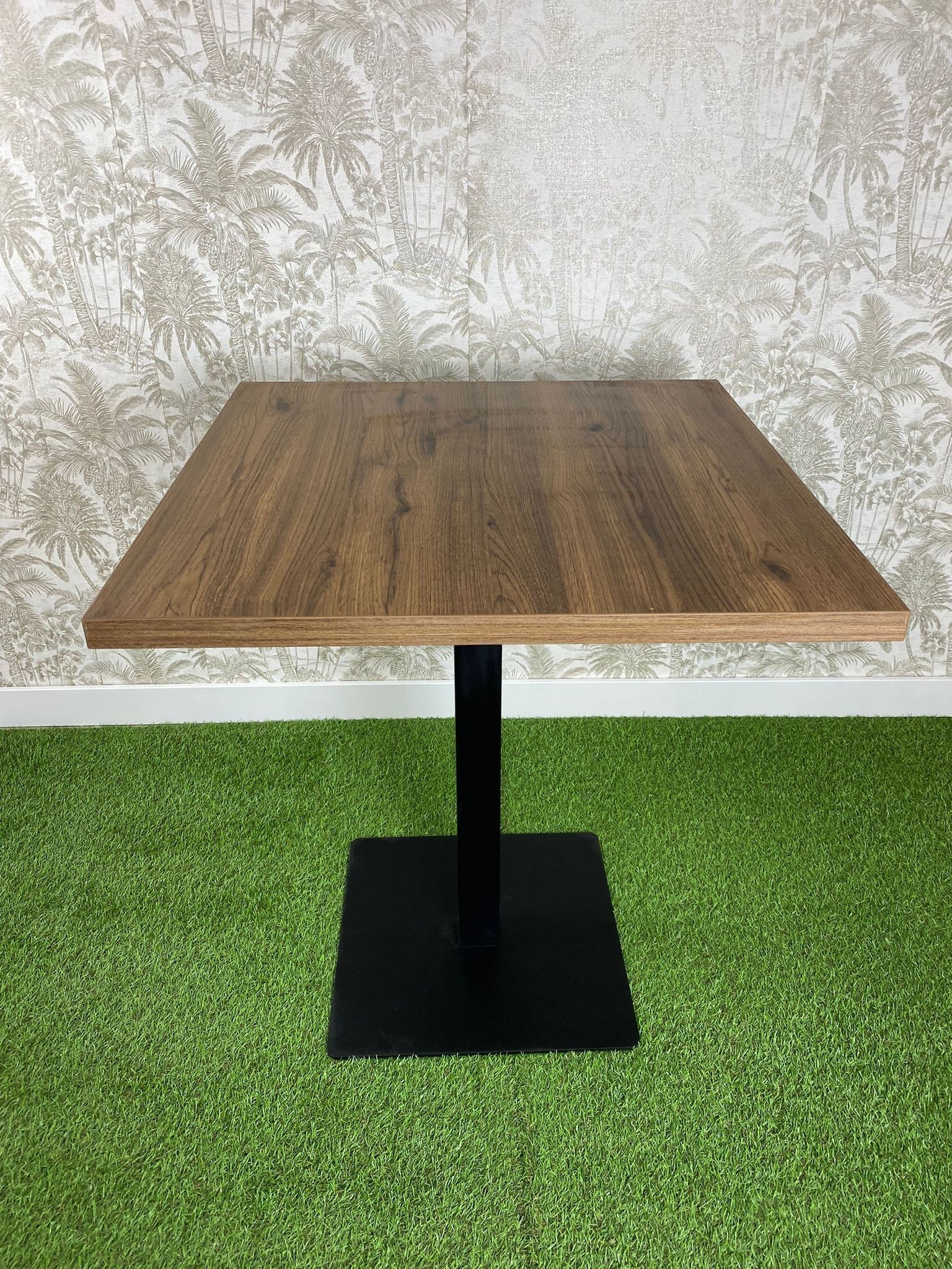 Una mesa de madera con una base negra está colocada encima de una alfombra verde.