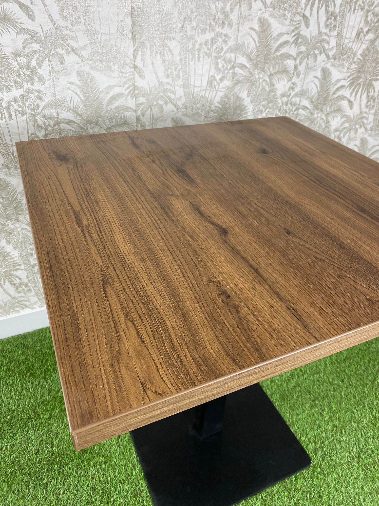 Una mesa de madera con una base negra está colocada encima de una alfombra verde.