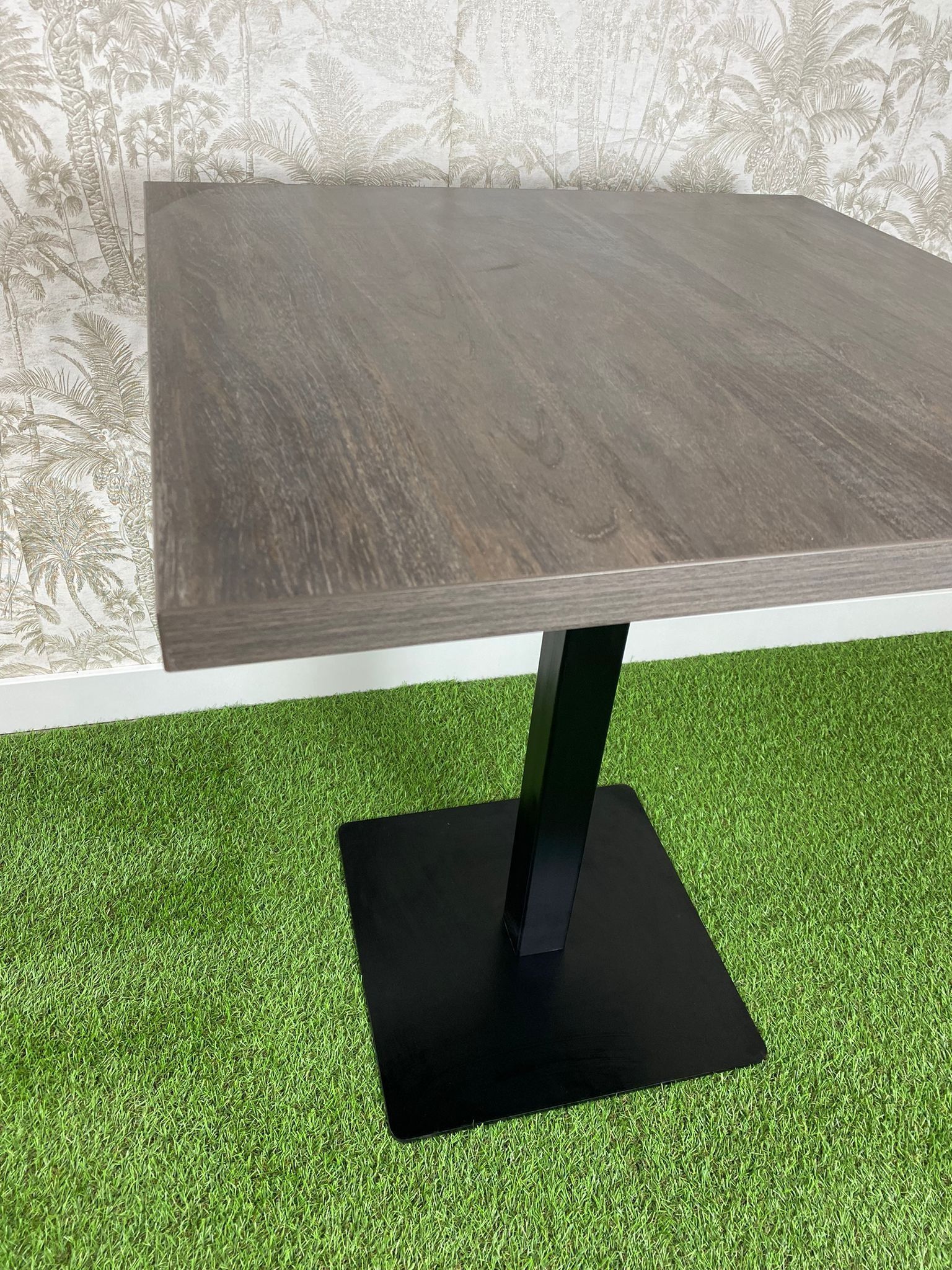 Una mesa cuadrada con una base negra se encuentra sobre un exuberante campo verde.