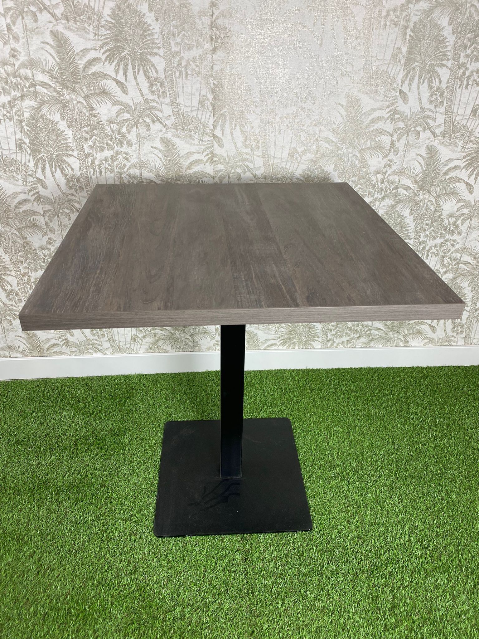 Una mesa cuadrada con una base negra se encuentra sobre un exuberante campo verde.