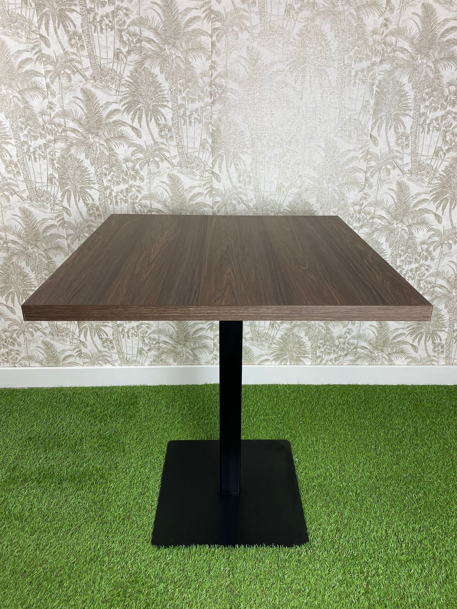 Una mesa cuadrada con una base negra se encuentra sobre un exuberante campo verde.