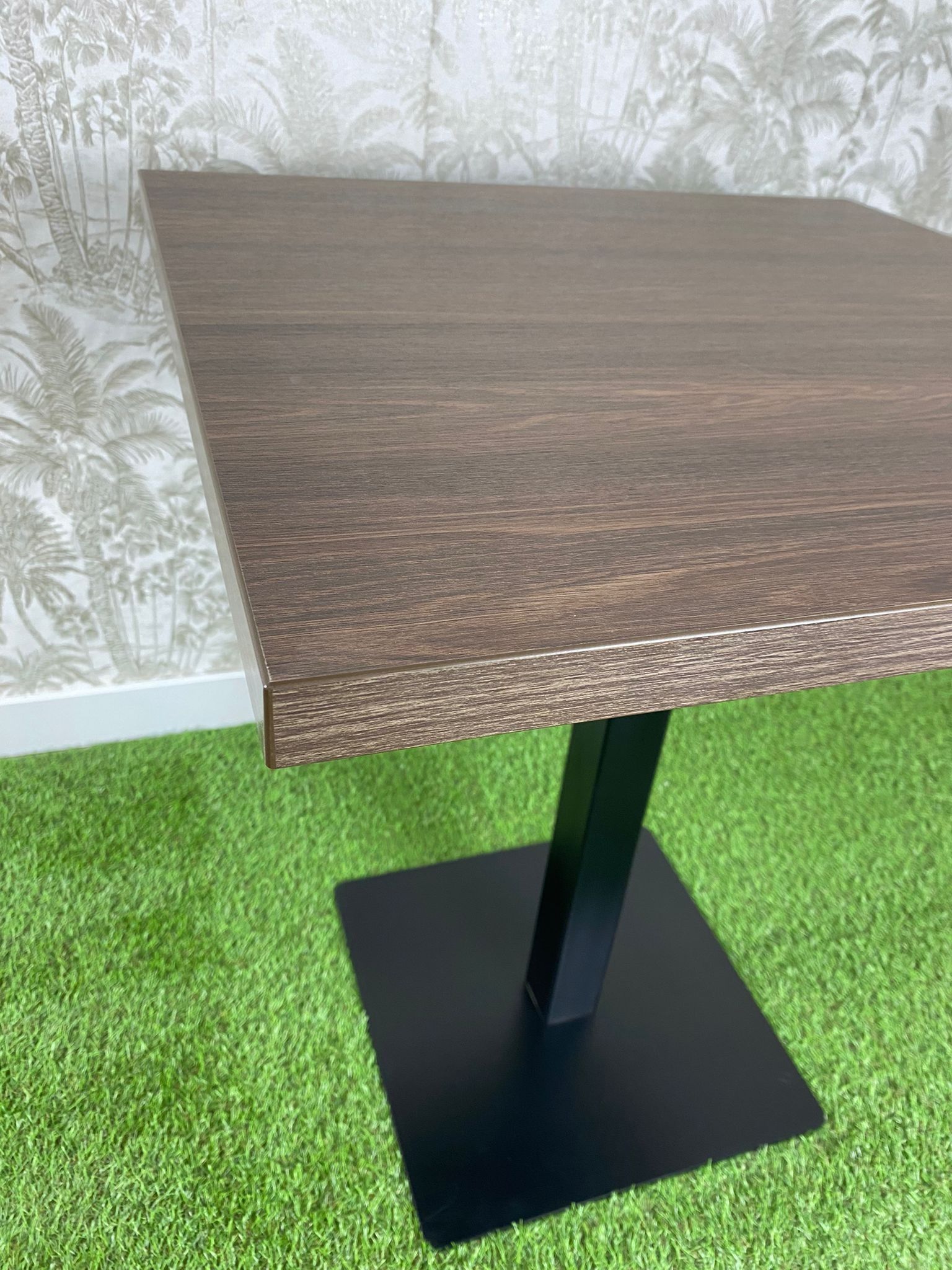 Una mesa cuadrada con una base negra se encuentra sobre un exuberante campo verde.