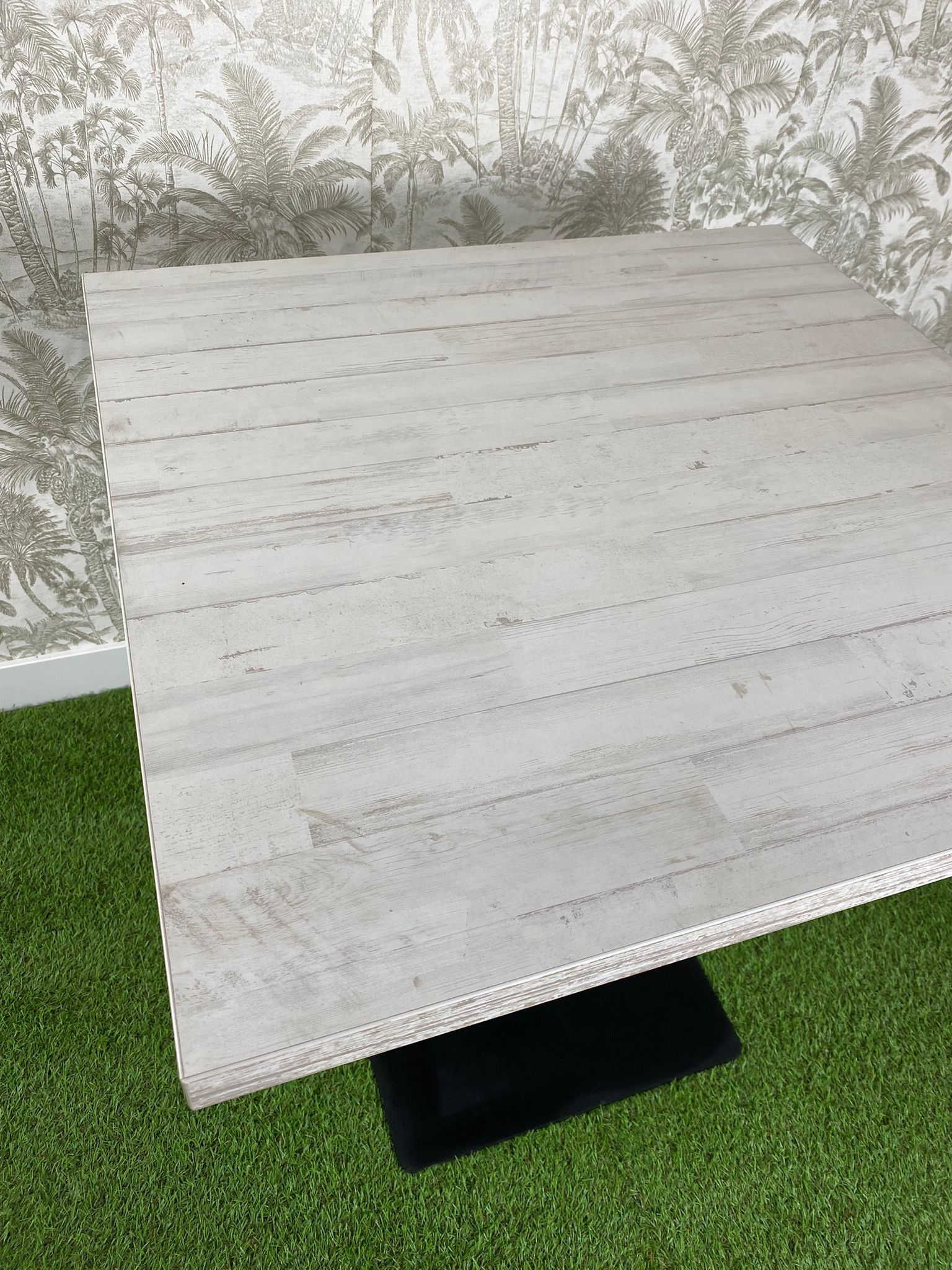 Una mesa cuadrada con una base negra reposa sobre una exuberante alfombra verde.