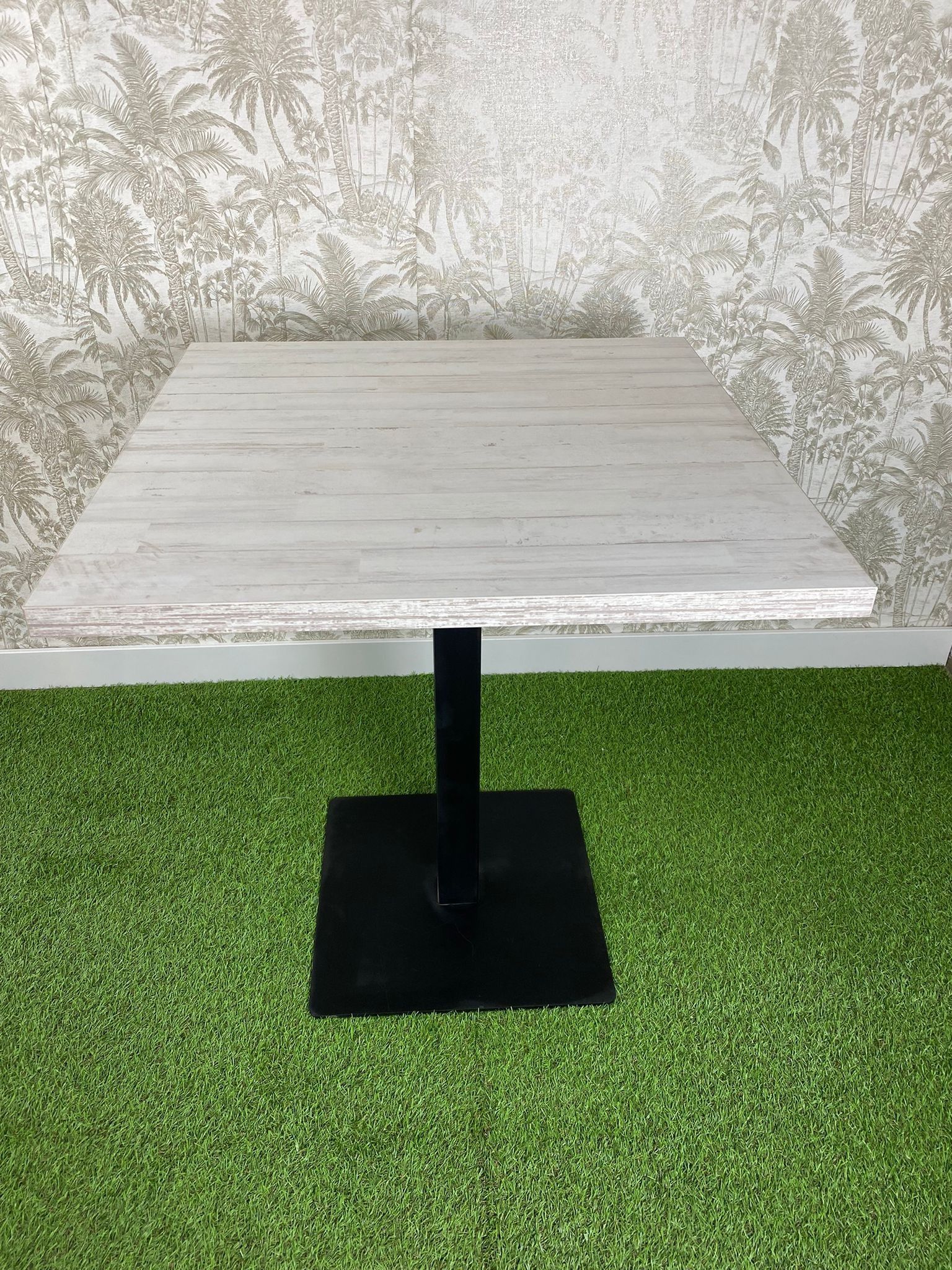 Una mesa cuadrada con una base negra reposa sobre una exuberante alfombra verde.