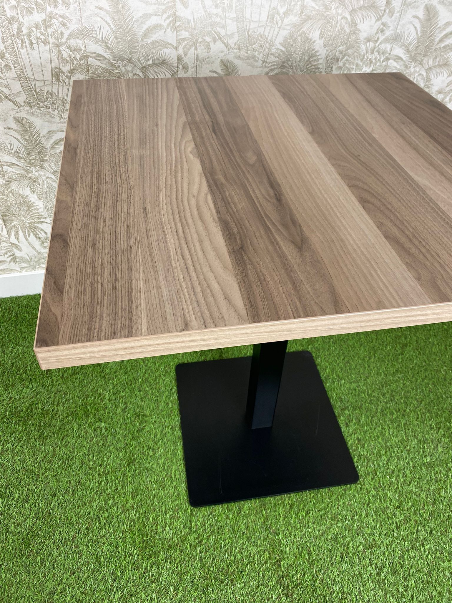 Una mesa de madera con una base negra está colocada encima de una alfombra verde.