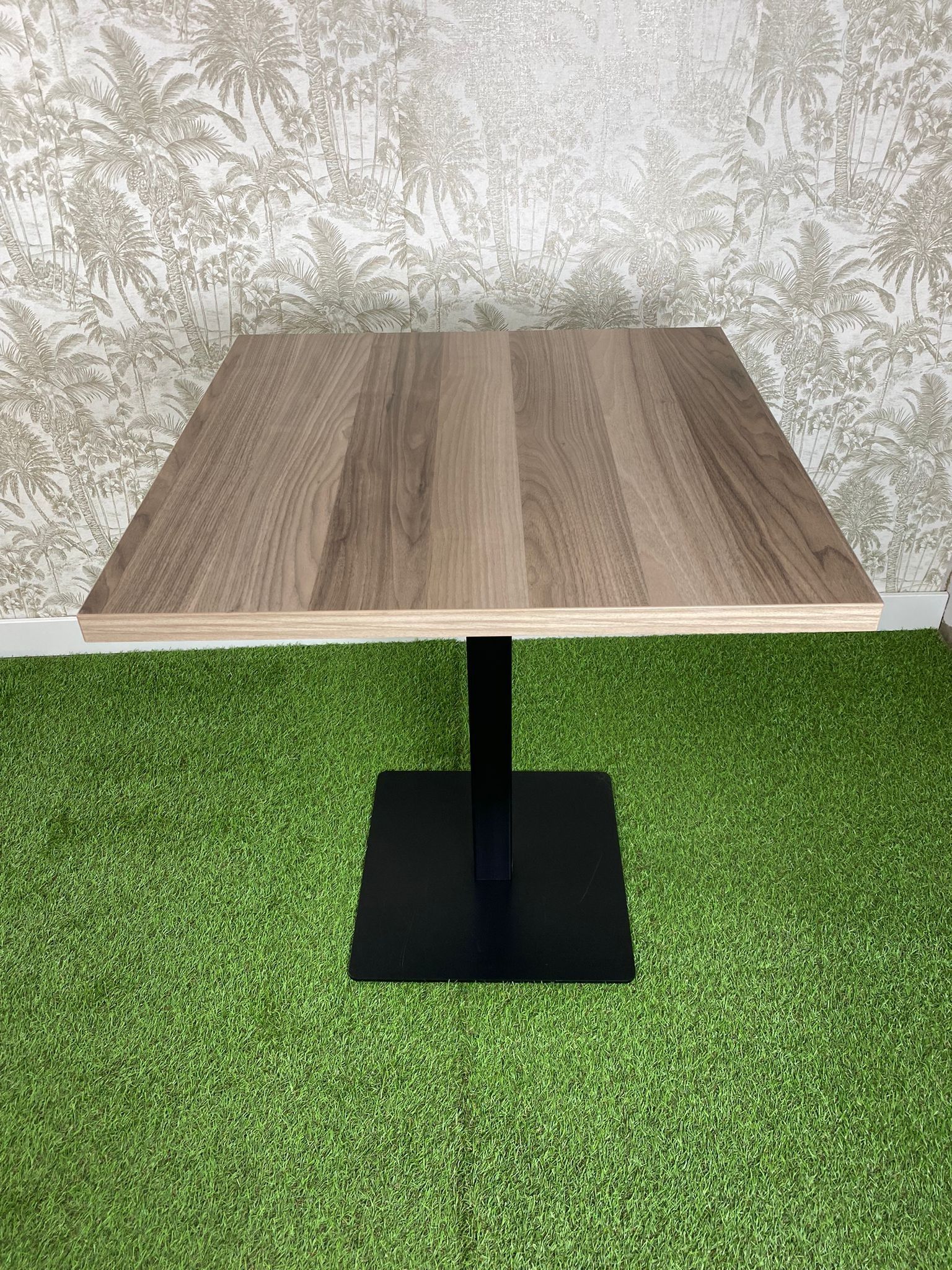 Una mesa de madera con una base negra está colocada encima de una alfombra verde.