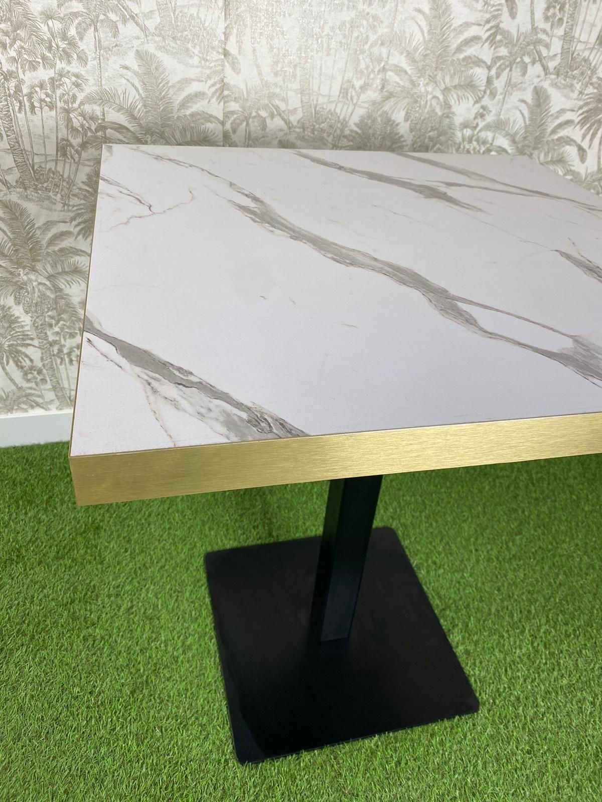 Una mesa cuadrada con tapa de mármol y detalles dorados se encuentra sobre un exuberante campo verde.