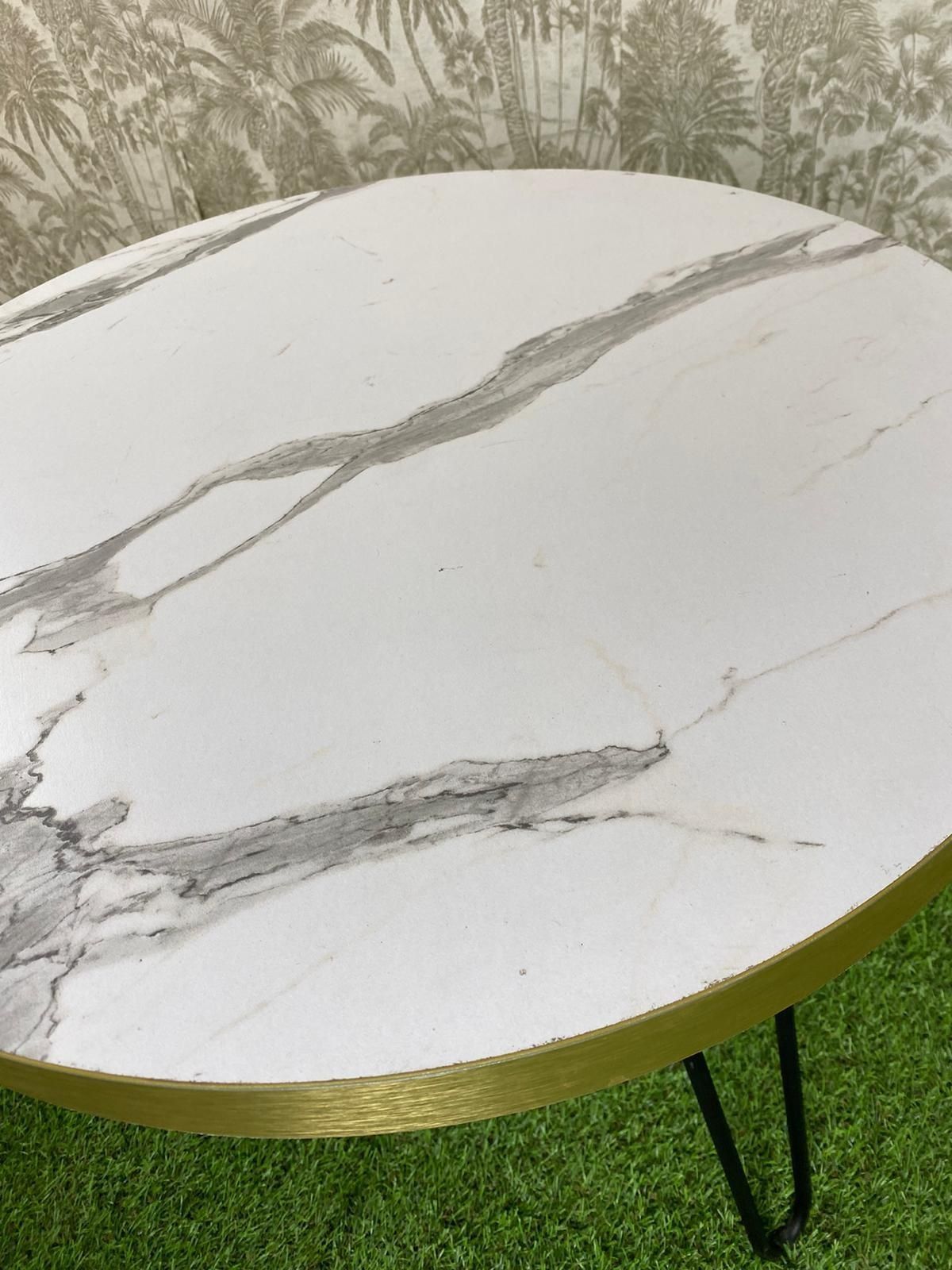 Una mesa redonda con tapa de mármol y patas de horquilla reposa sobre una alfombra verde.
